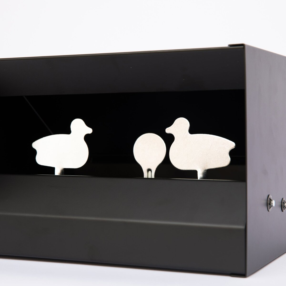 A black box with three white metal cutouts of ducks and a circle. The background is black, and the base is black.