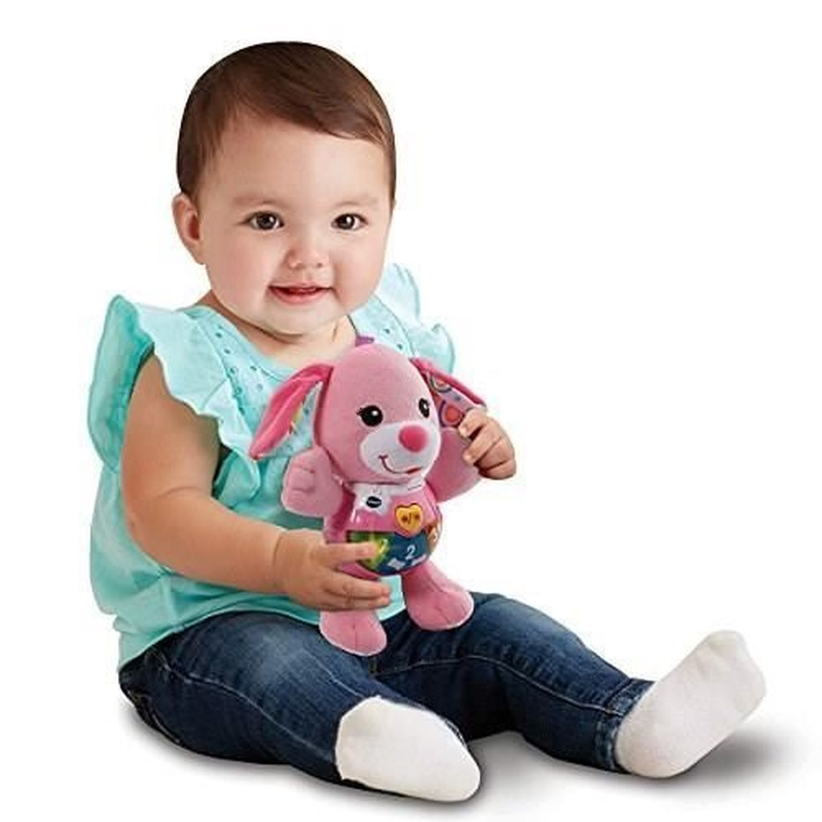 Ein Baby sitzt und hält ein rosa Hundespielzeug. Das Baby trägt ein blaues Hemd und Jeans. Der Hintergrund ist weiß.