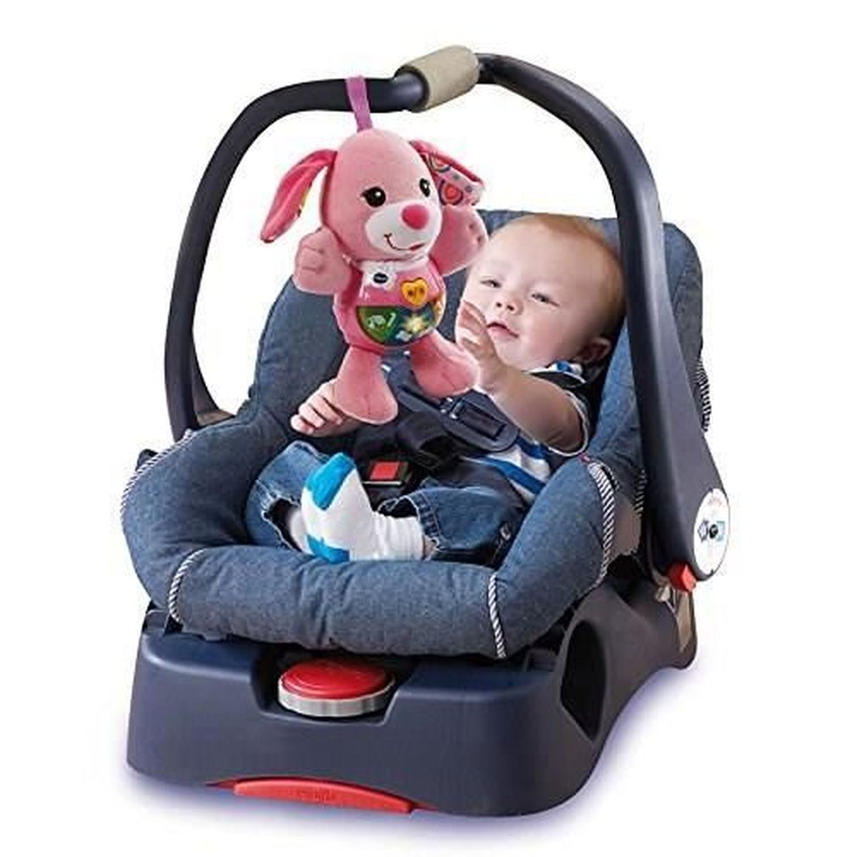 Ein Baby sitzt in einem Autositz mit einem rosa Hundespielzeug darüber. Das Baby trägt Jeans und ein gestreiftes Hemd.