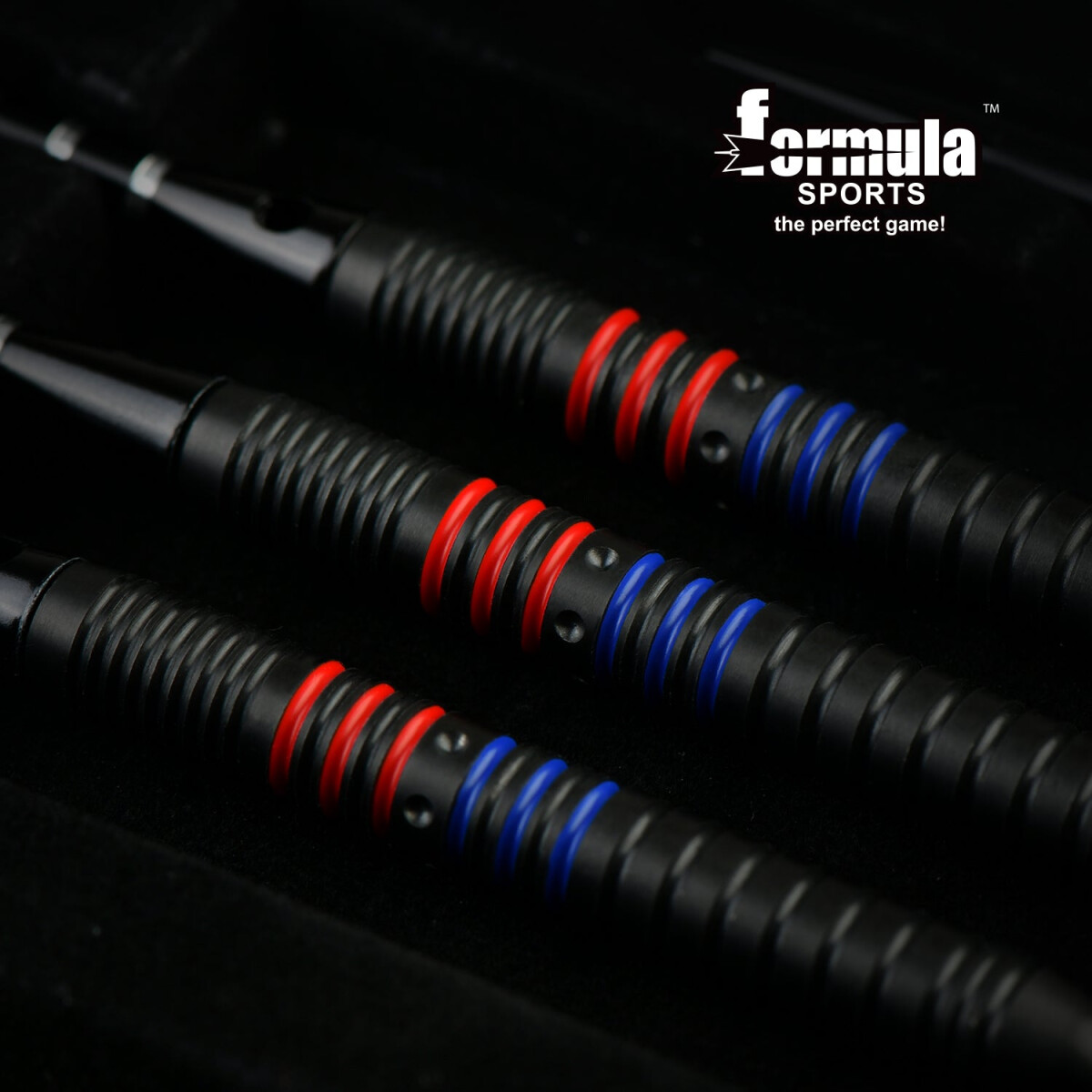 Nahaufnahme von drei schwarzen Darts mit roten und blauen Ringen. Die Darts sind diagonal auf dunklem Hintergrund angeordnet.