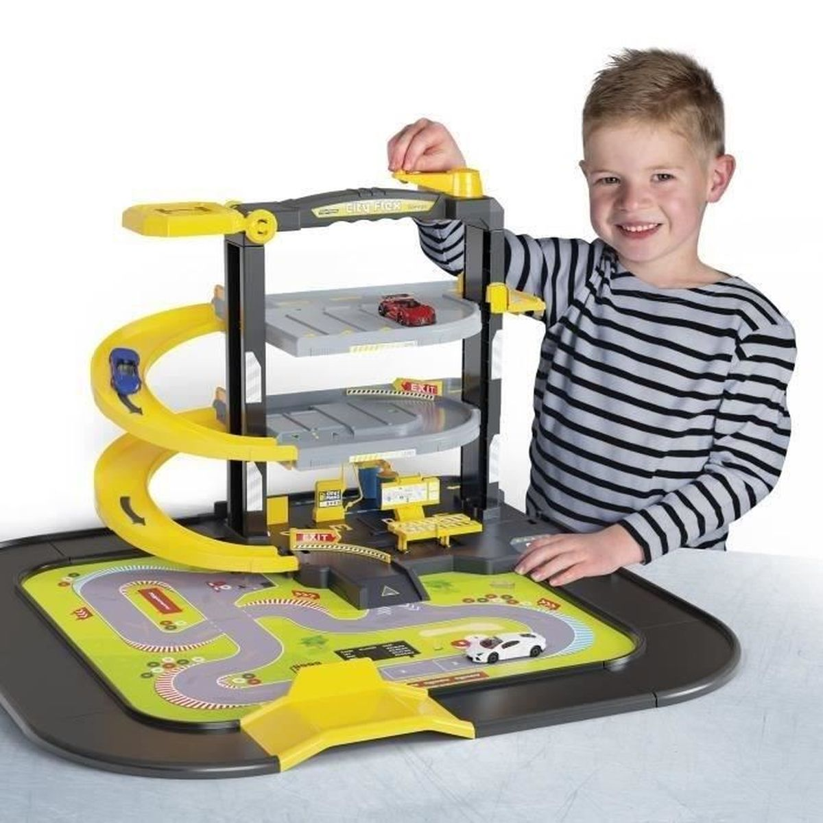 Ein Junge lächelt und spielt mit einer Spielzeug-Autogarage. Die Garage hat Rampen und Parkebenen. Autos befinden sich auf den Rampen und Ebenen.