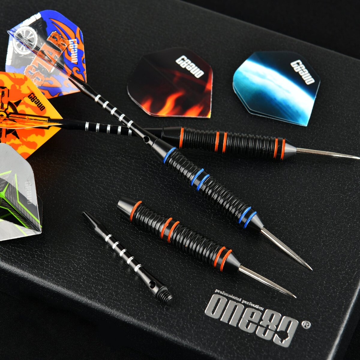 Darts mit verschiedenfarbigen Flights und schwarzen Barrels mit blauen und orangen Ringen, auf dunkler Oberfläche.