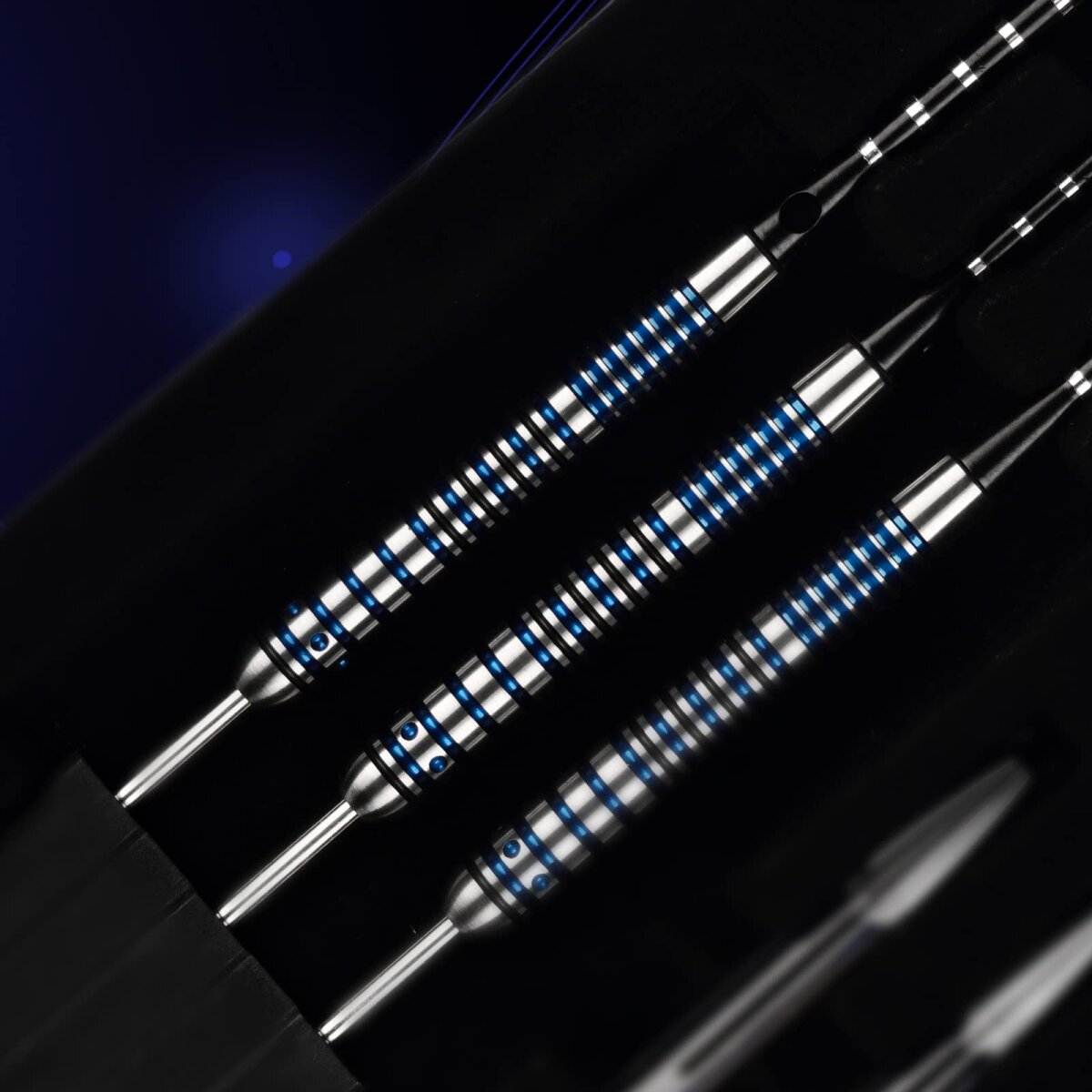 Close-up of four darts with silver, blue, and black accents, arranged diagonally against a dark background.