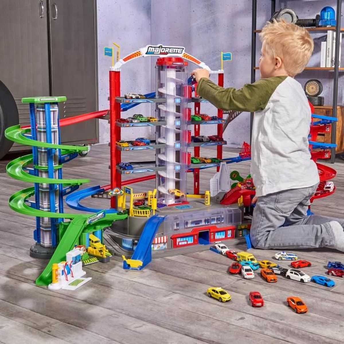 Ein Kind spielt mit einer Spielzeuggarage. Die Garage ist bunt mit Rampen und einer Spirale. Viele Spielzeugautos liegen auf dem Boden.