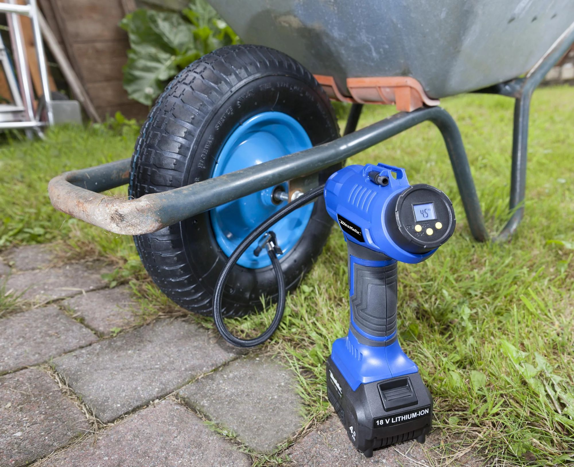 Eine blaue Luftpumpe neben einem Schubkarrenrad auf Gras. Die Pumpe zeigt 4,5 an. Der Hintergrund ist unscharf.