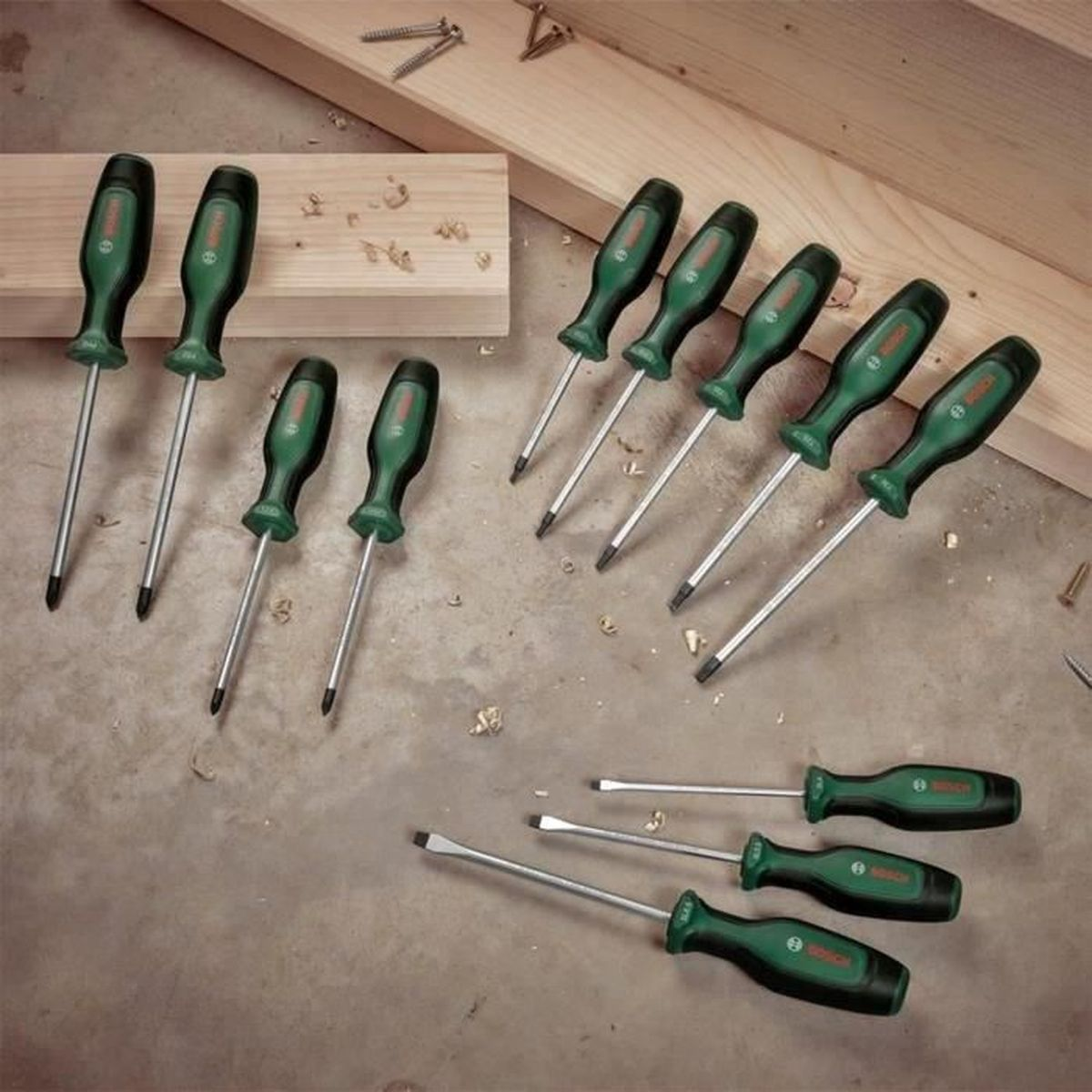 L'immagine mostra una collezione di cacciaviti verdi e neri su una superficie con legno e viti. Sono presenti diversi tipi e dimensioni.