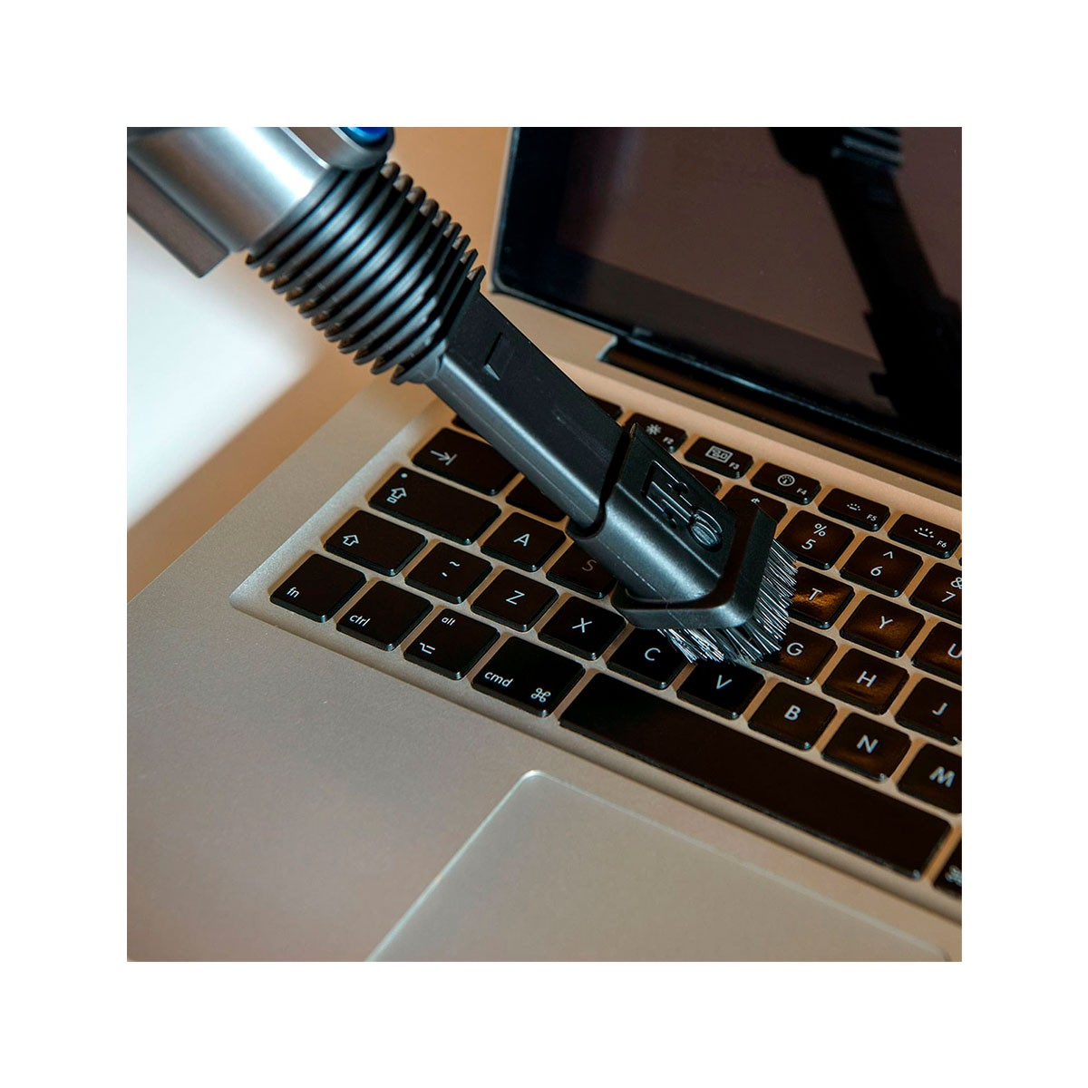 Una tastiera di un laptop pulita con un piccolo aspirapolvere. La tastiera ha tasti neri, il pulitore è nero e argento.