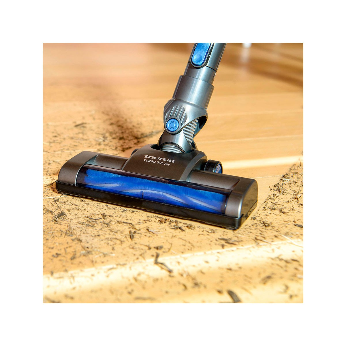 Un aspirapolvere Taurus Turbo Brush pulisce un pavimento in legno. La spazzola è nera e blu. Detriti sono visibili sul pavimento.