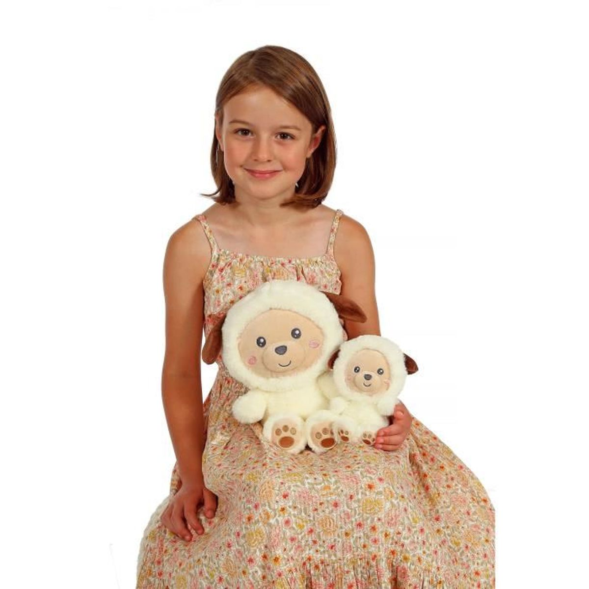 Ein Mädchen in einem geblümten Kleid hält zwei Schaf-Plüschtiere. Die Schafe sind cremefarben mit braunen Akzenten. Das Mädchen lächelt in die Kamera.