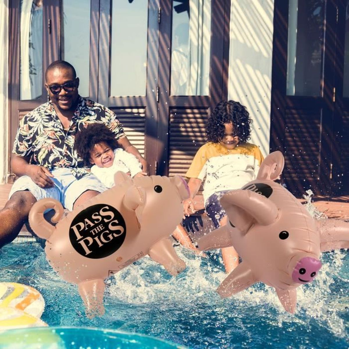 Una famiglia gioca con maiali gonfiabili in piscina. Un uomo e due bambini sono nella scena. L'acqua schizza intorno ai maiali.