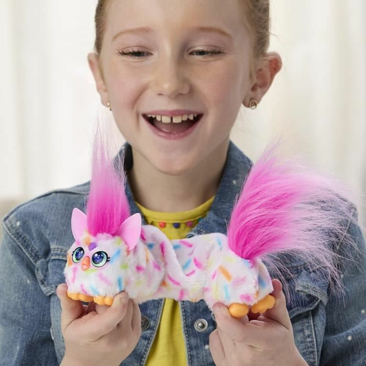 Ein lächelndes Mädchen hält ein buntes Spielzeug. Das Spielzeug hat rosa Haare und einen Schwanz, mit einem weißen Körper mit bunten Streuseln.