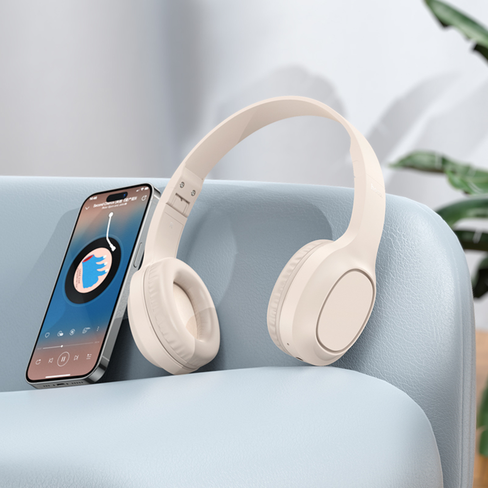Cuffie beige e uno smartphone su un divano blu. Il telefono mostra un'interfaccia musicale. Sullo sfondo c'è una pianta verde.