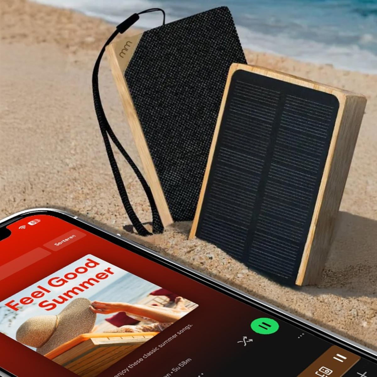Een telefoon met een zomerse afspeellijst op een zandstrand, met twee houten luidsprekers. Eén is een zonnelader.