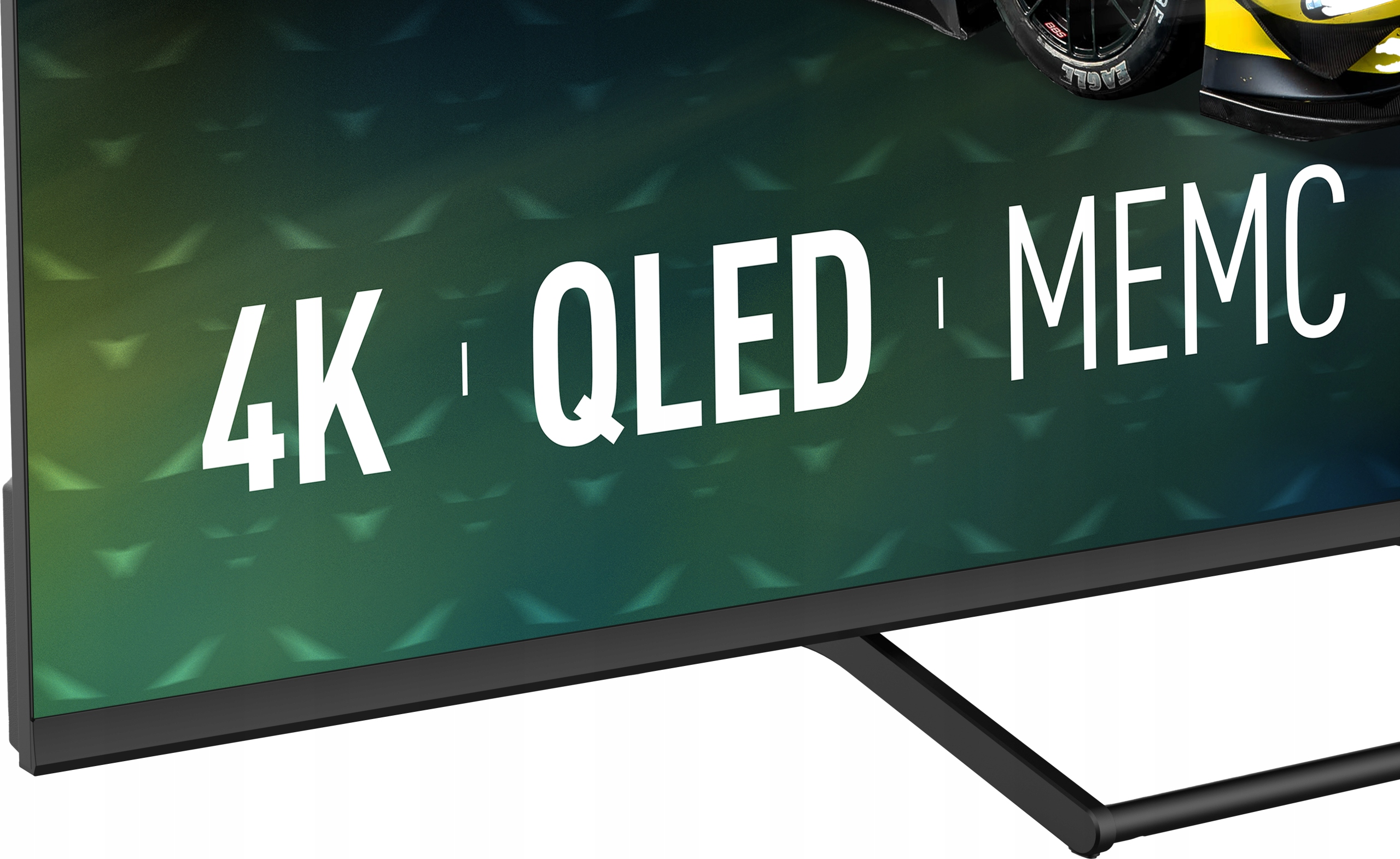 Ekran telewizora wyświetla '4K QLED MEMC'. Koło samochodu widoczne u góry. Tło jest zielone z wzorem rombów.