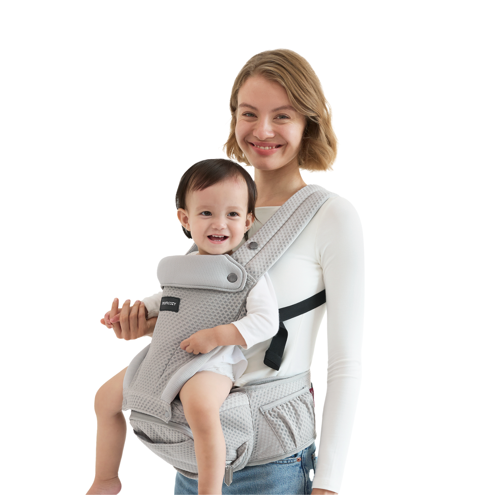 A woman holds a baby in a gray baby carrier. Both are smiling. The background is white.