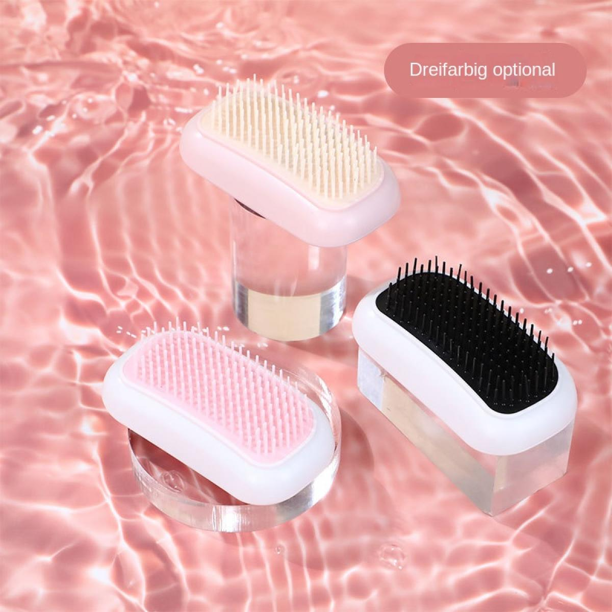 Drei Haarbürsten mit unterschiedlich farbigen Borsten auf einer rosa Oberfläche mit Wasserwellen.