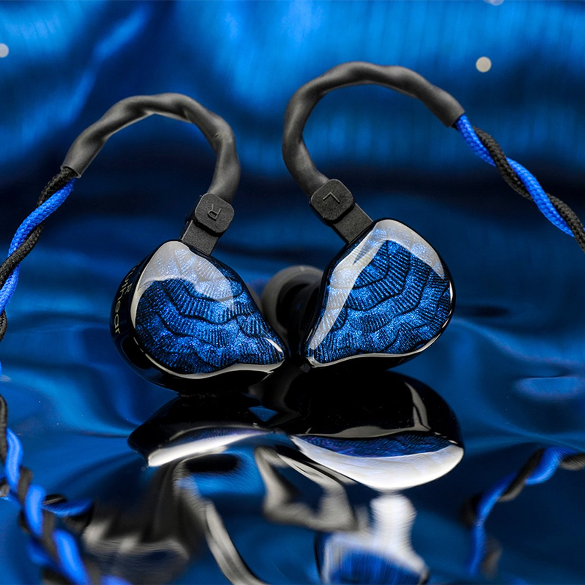 Twee in-ear oortelefoons met blauwe en zwarte kabels liggen op een reflecterend blauw oppervlak. De oortelefoons zijn blauw met een gedetailleerd patroon.