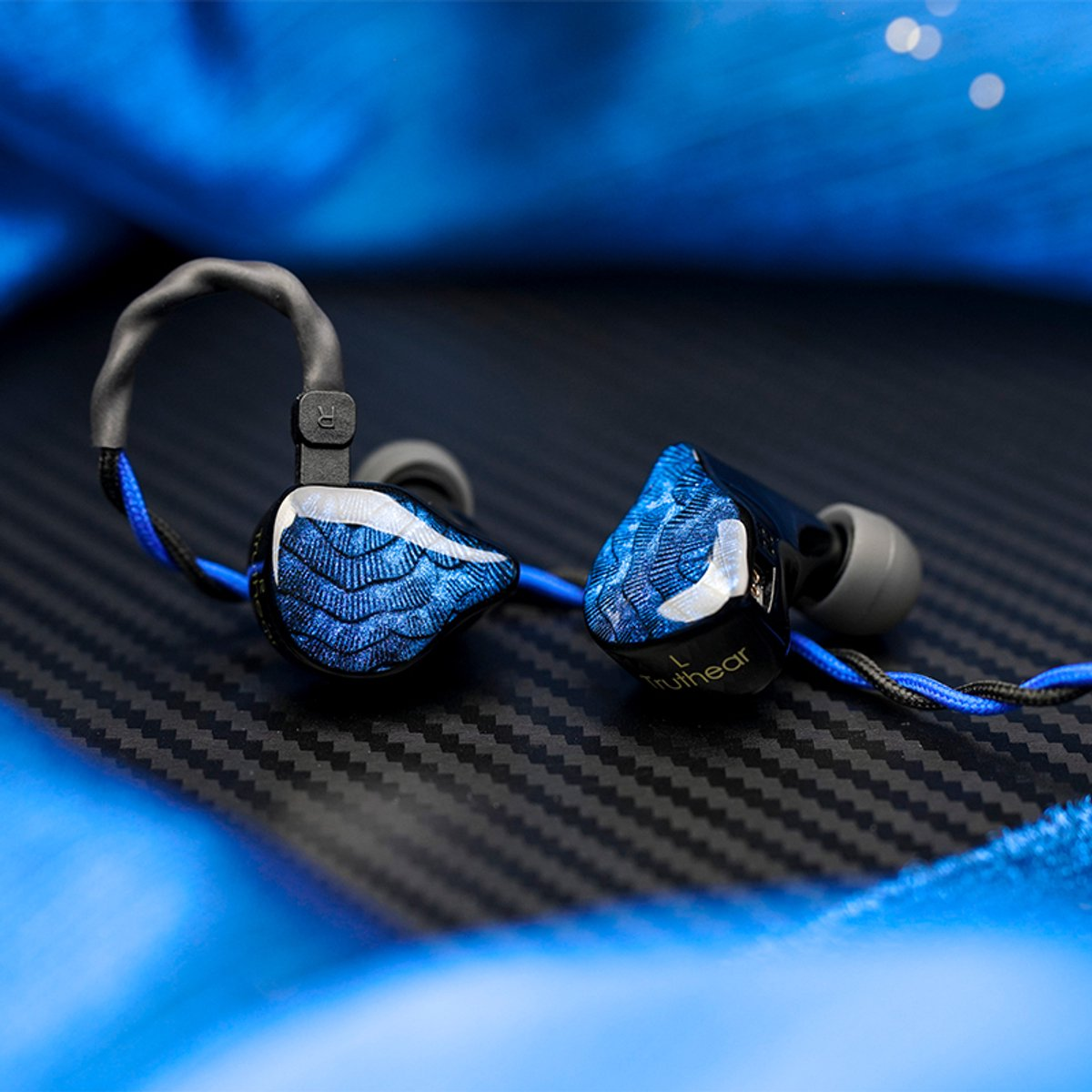 Twee in-ear-hoofdtelefoons met blauw en zwart design liggen op een getextureerd donker oppervlak. De achtergrond is blauw vervaagd.
