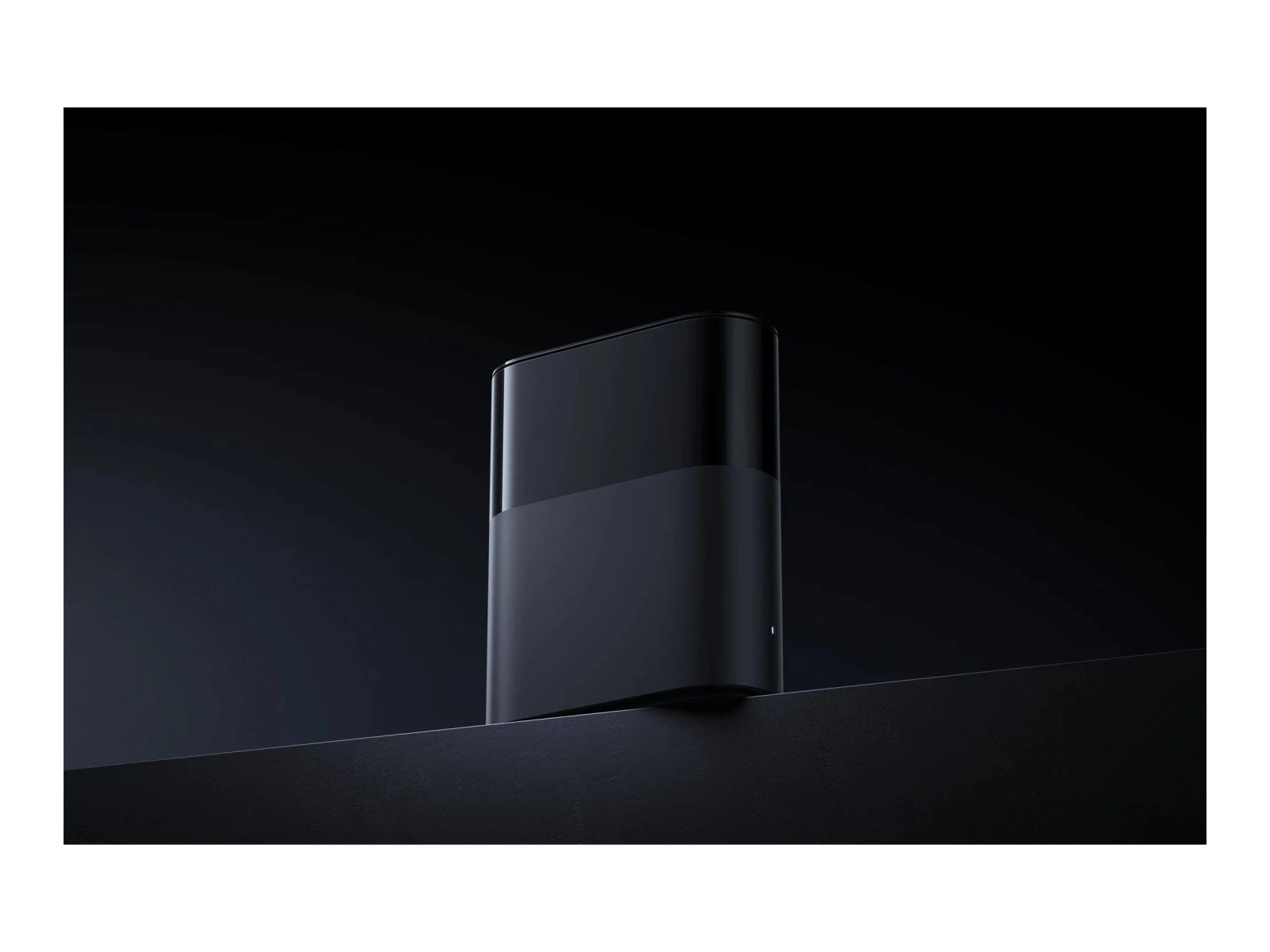 A sleek, black rectangular device stands on a dark surface against a black backdrop. It has a two-tone design.