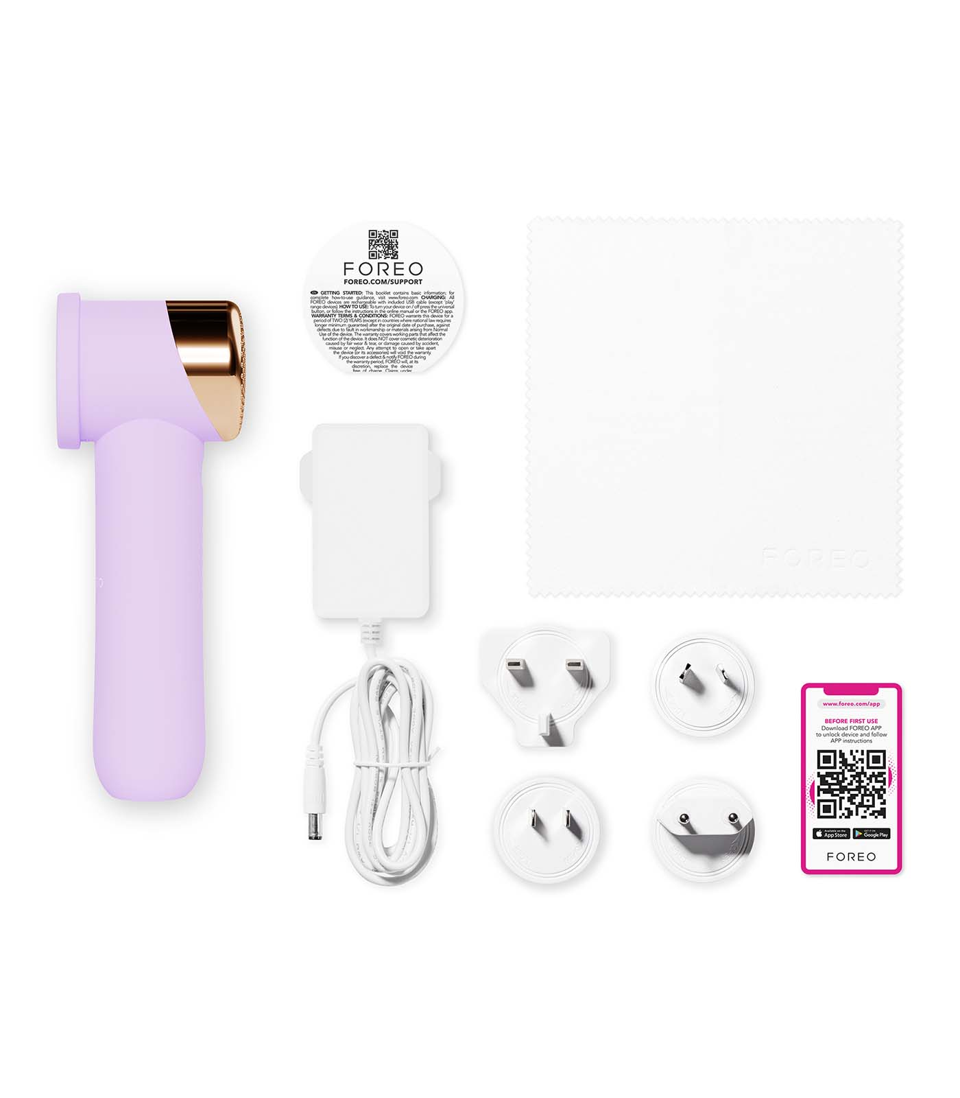 A Foreo skincare device with accessories: charger, adapters, cloth, and instructions. The device is lavender with a gold head.