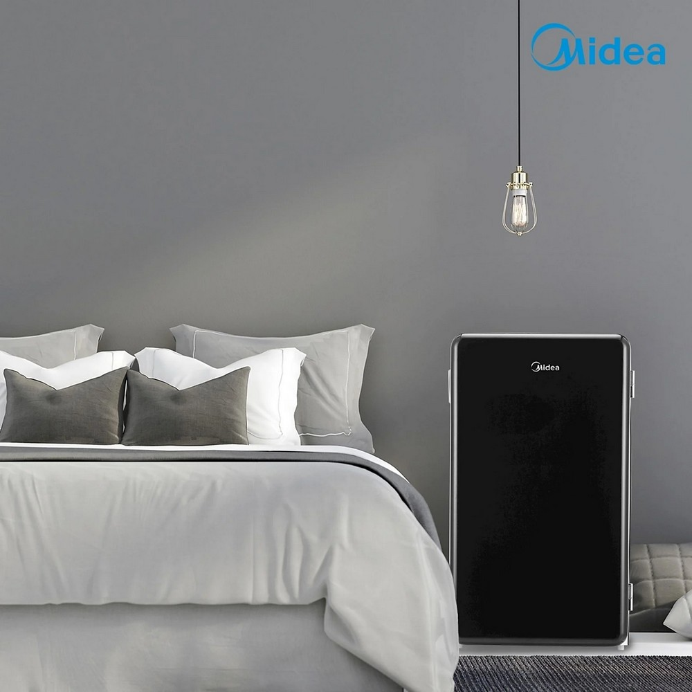 Una scena di camera da letto con un letto e un mini-frigorifero nero. Una lampada pende dal soffitto. Visibile un logo Midea.