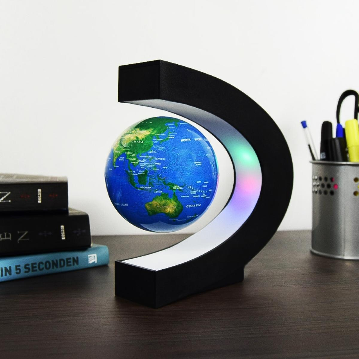 Een zwevende wereldbol, met een zwart frame en een kleurveranderend licht. Boeken en pennen zijn zichtbaar op een houten bureau.