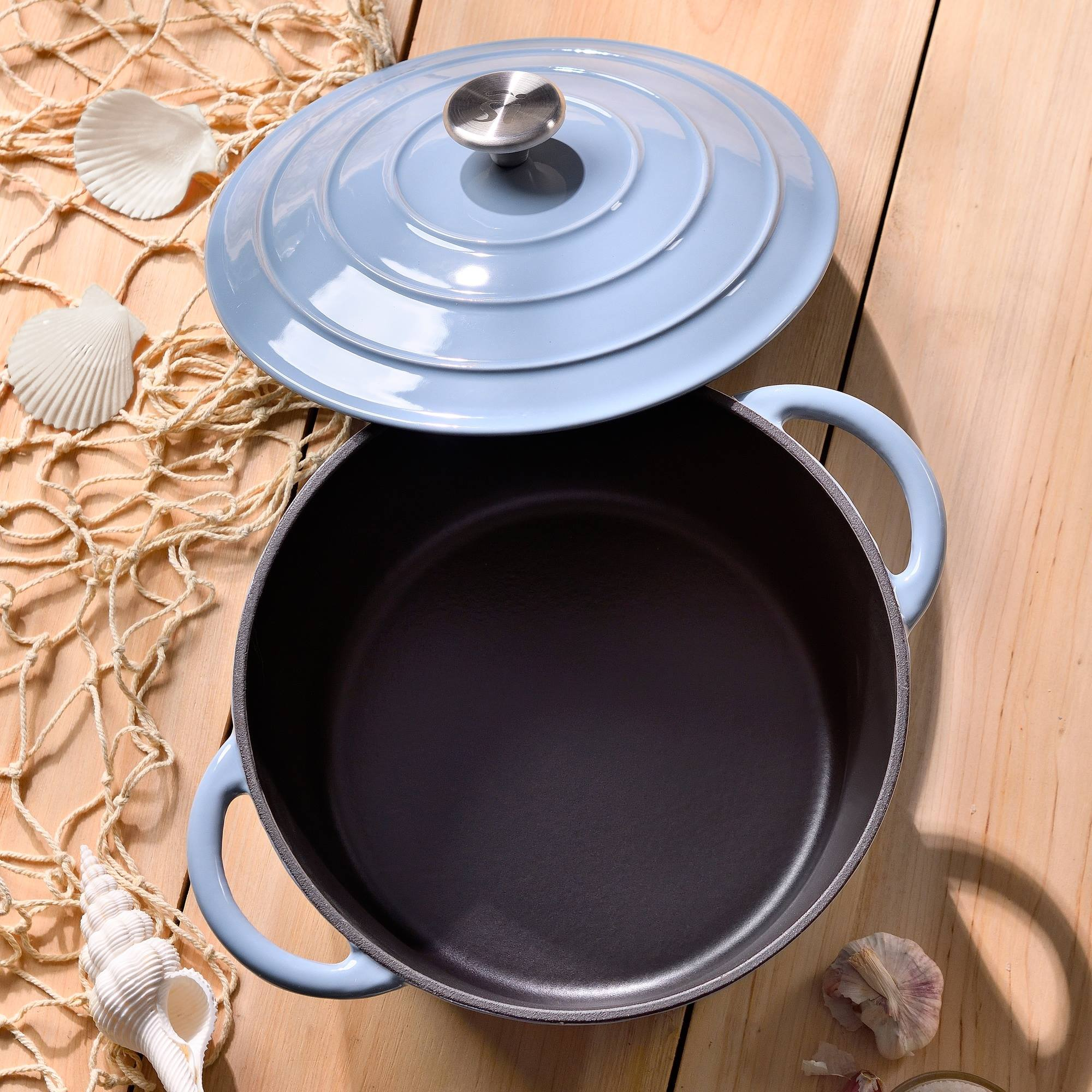 Una olla azul claro con tapa, conchas marinas y red de pesca sobre una superficie de madera.
