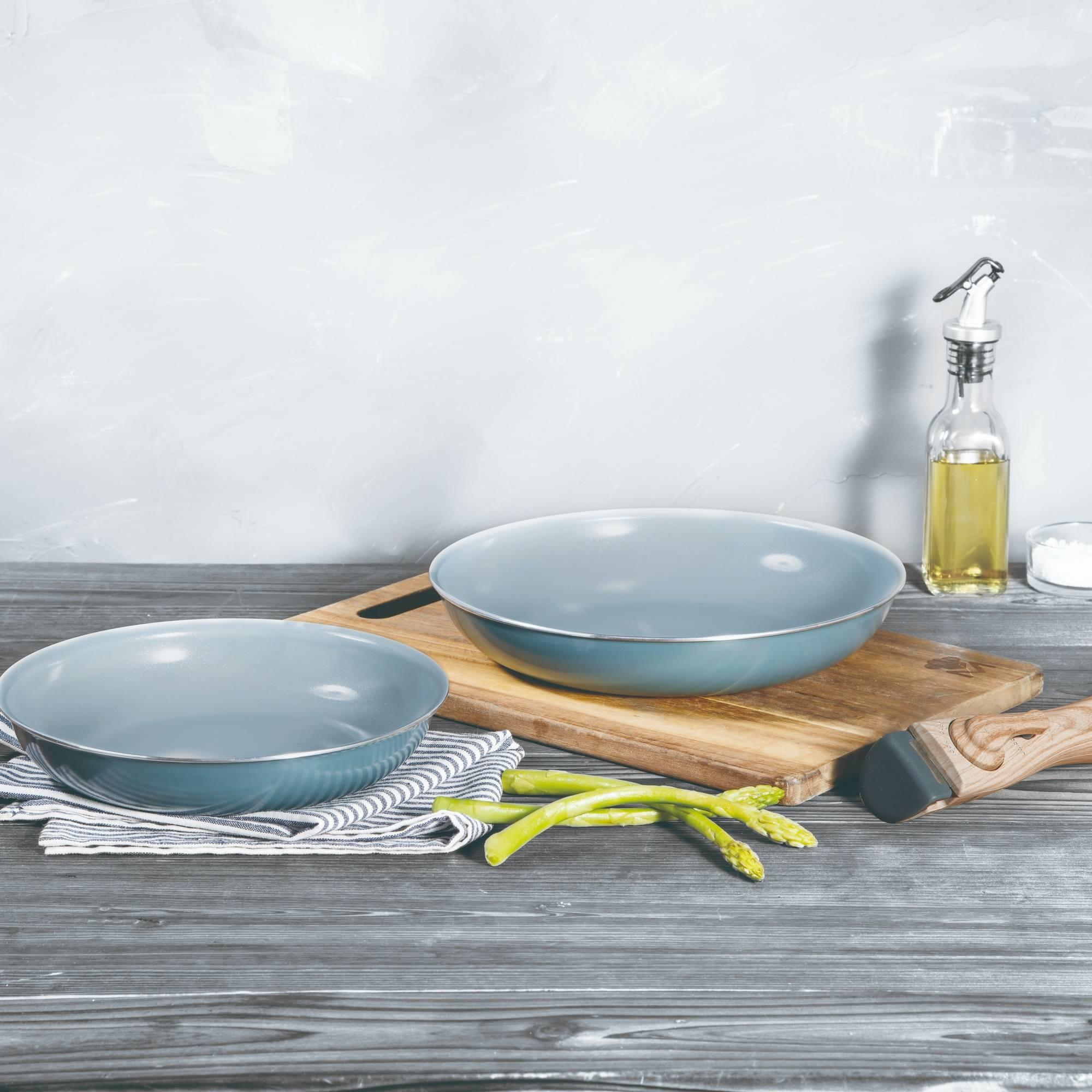 Dos cuencos azules sobre una tabla de madera con espárragos, botella de aceite y un rallador sobre una mesa de madera.