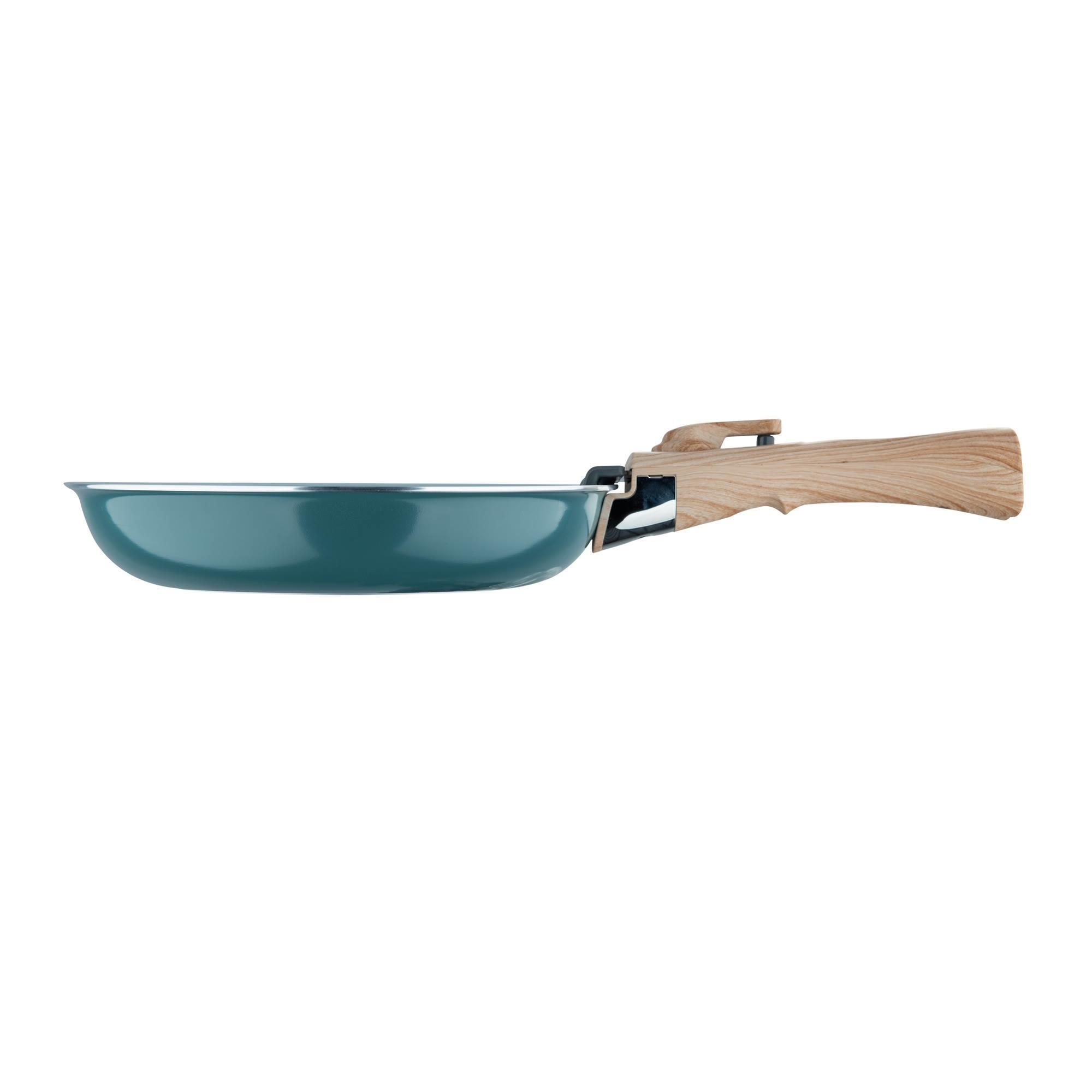 Una sartén verde azulado con mango de madera se ve de lado. El fondo es blanco.