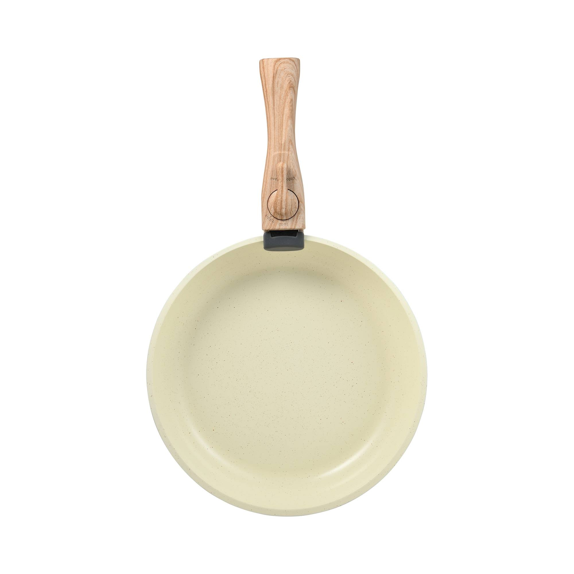Vista cenital de una sartén clara con mango de madera, sobre un fondo blanco.