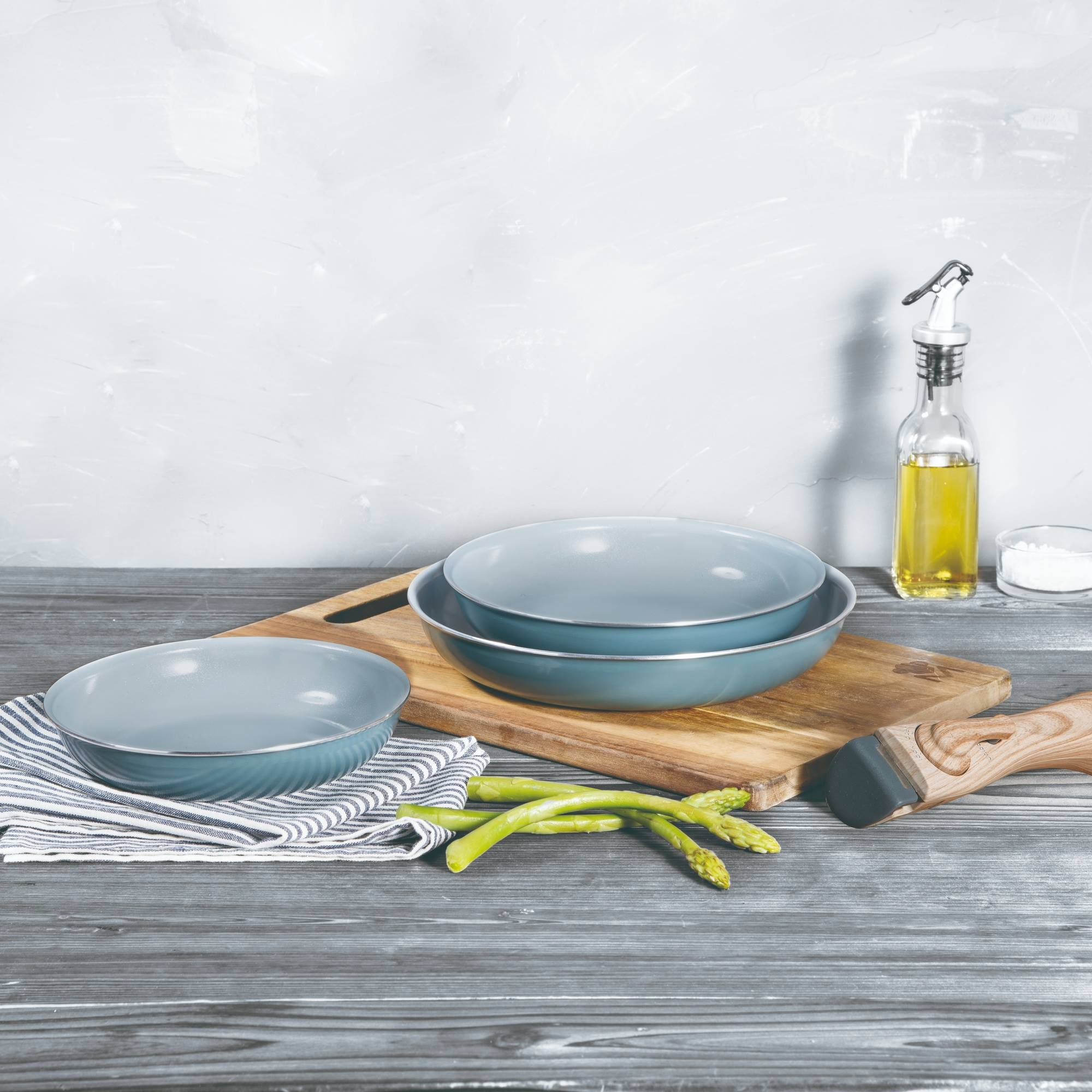 Una escena de cocina con cuencos, espárragos, botella de aceite y tablas de cortar sobre una mesa de madera.