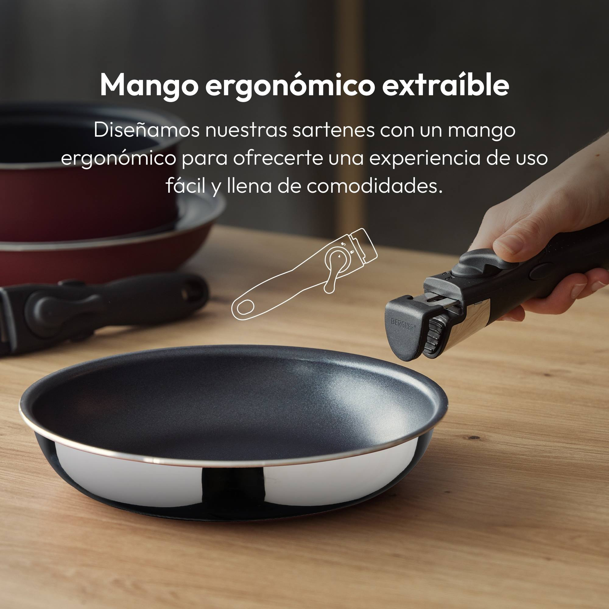 Una sartén con mango extraíble, una mano sosteniendo el mango y otra sartén al fondo, todo sobre una superficie de madera.