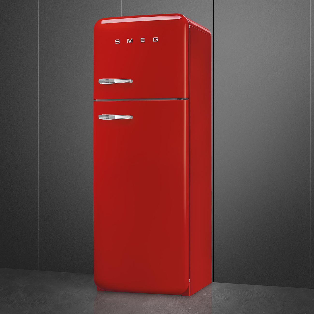 Un refrigerador rojo SMEG se encuentra sobre un piso gris contra una pared gris oscura. Tiene dos puertas y manijas cromadas.