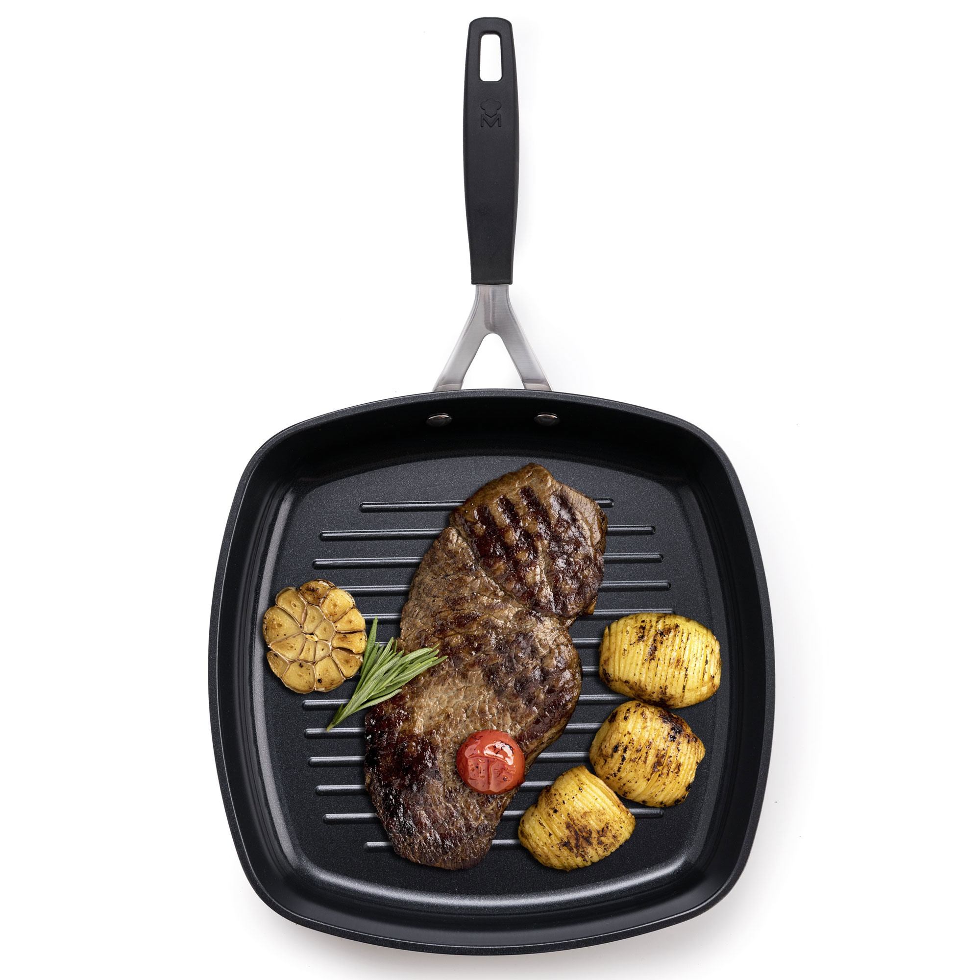 Un bistec a la parrilla con patatas asadas, ajo y tomate en una sartén, con mango negro, sobre fondo blanco.
