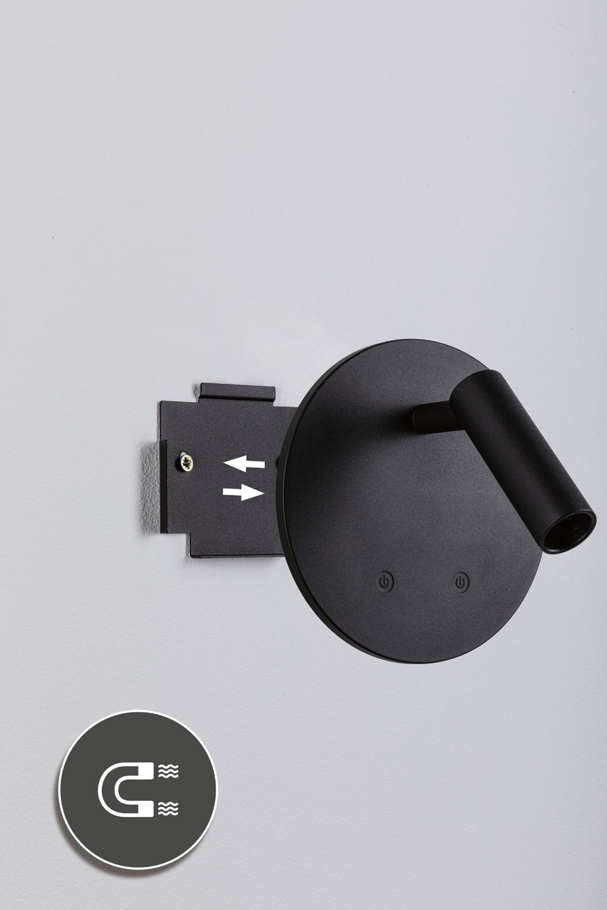 Schwarze Wandleuchte mit rundem Kopf und abgewinkeltem Arm, an einer grauen Wand befestigt. Unten befindet sich ein Magnetsymbol.