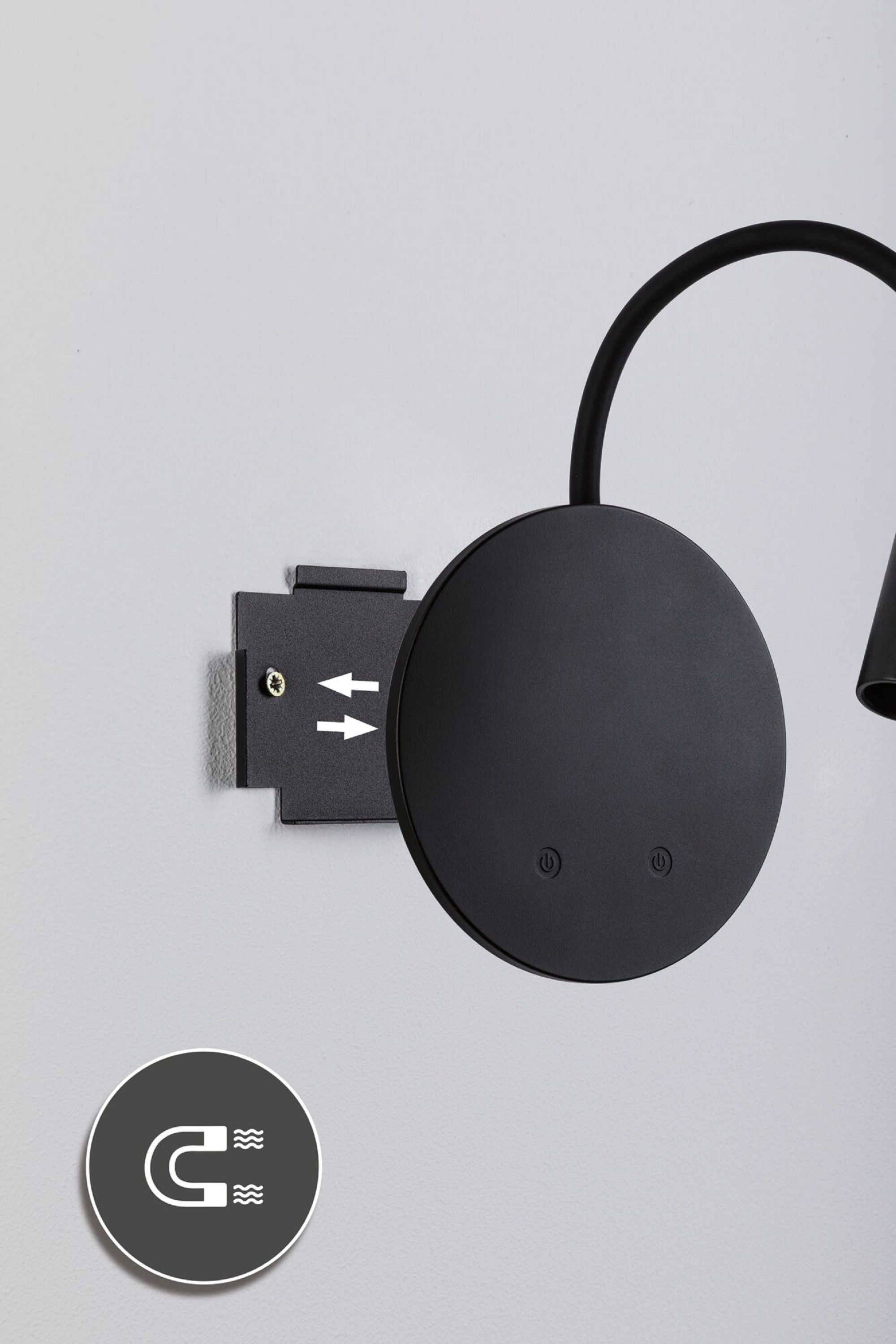 Eine schwarze Lampe mit rundem Kopf und gebogenem Arm. Sie ist an der Wand befestigt, magnetisch.