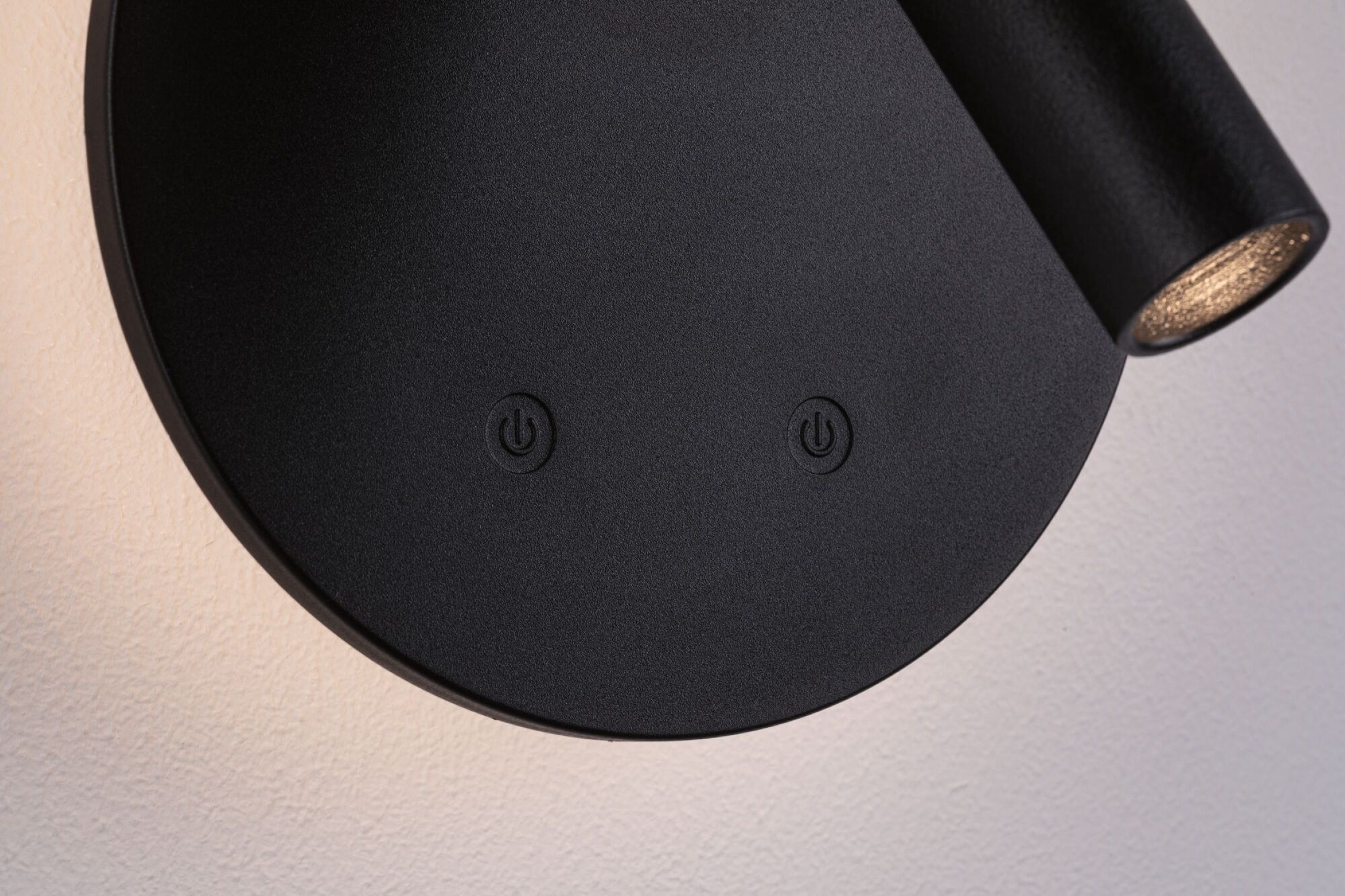 Zbliżenie czarnej lampy z okrągłą podstawą i regulowanym światłem. Symbole zasilania są widoczne na podstawie.