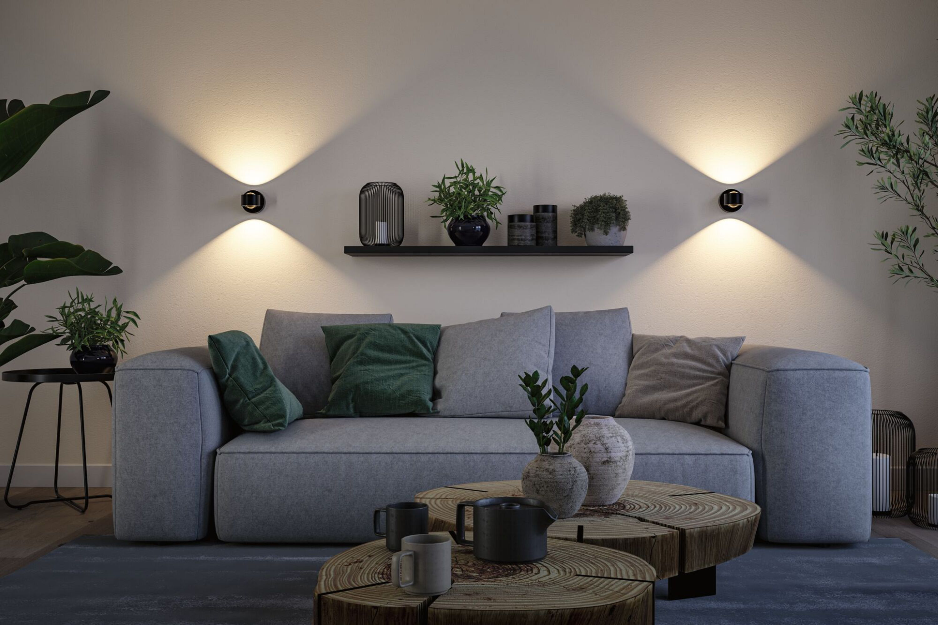 Nowoczesny salon z szarą sofą, roślinami i drewnianymi stołami. Kinkiety oświetlają przestrzeń.