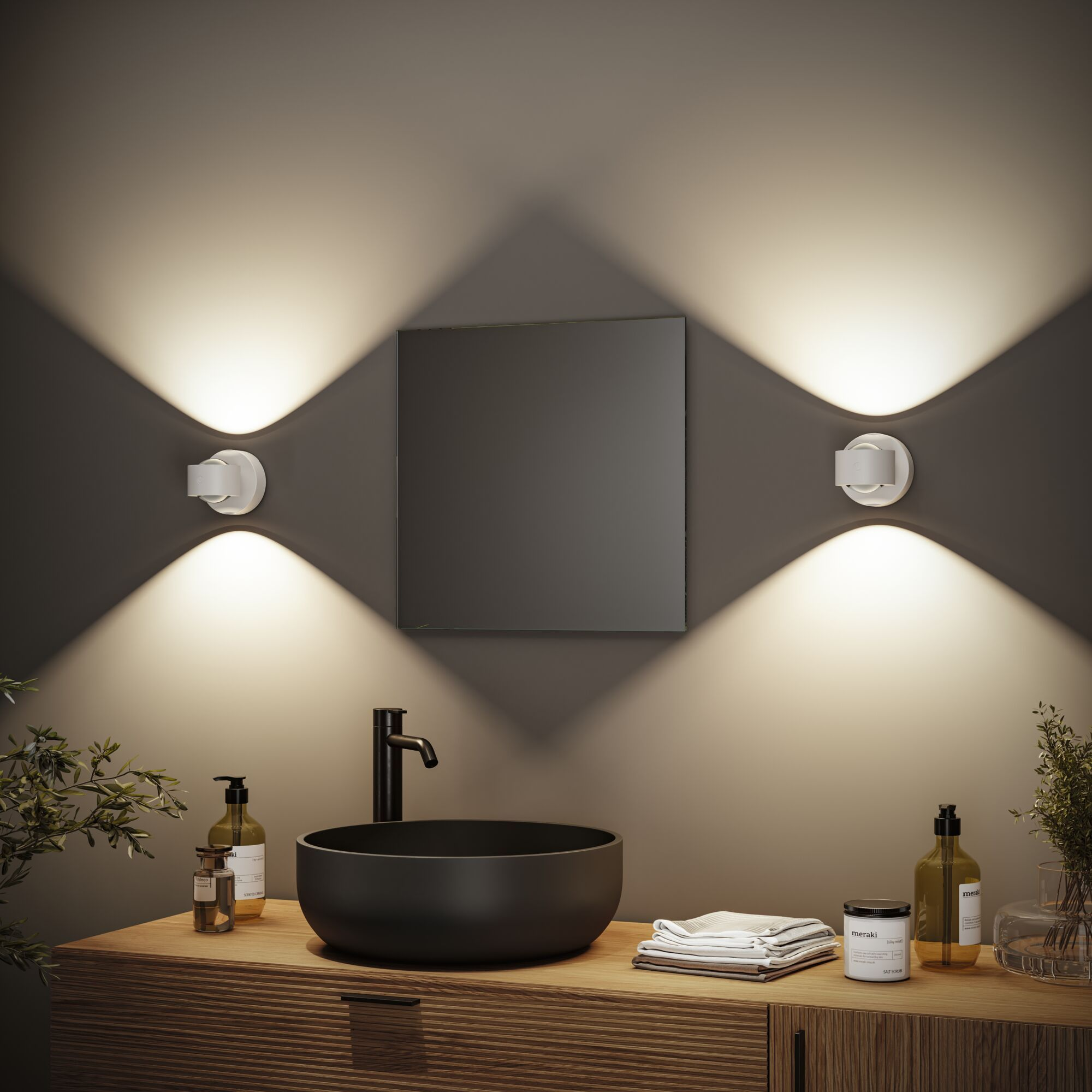 Łazienka z umywalką, lustrem i dwoma kinkietami. Drewniana szafka z mydłem, ręcznikami i dekoracjami. Czarny kran.