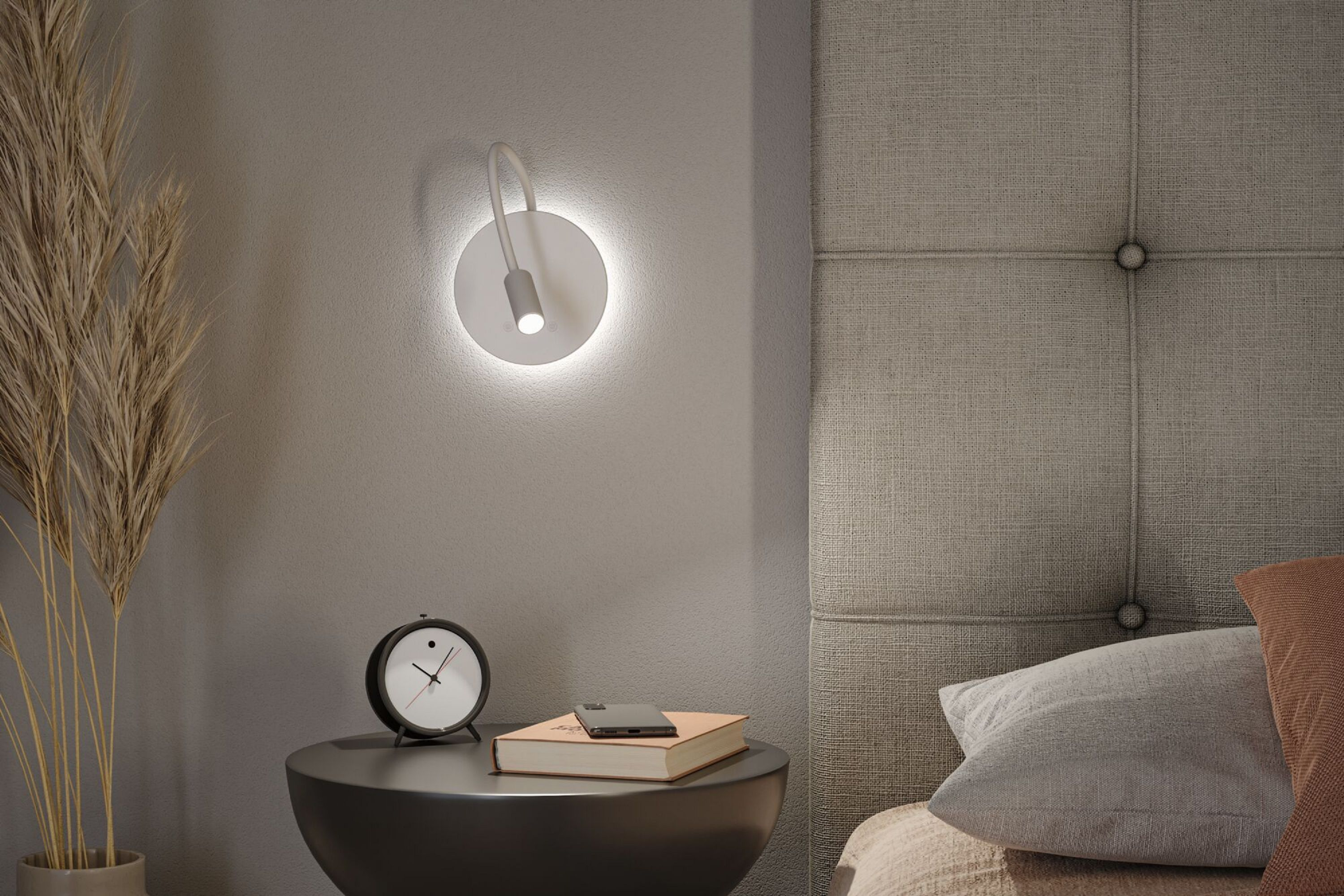 Scena sypialni z stolikiem nocnym, lampą, zegarem, książką, telefonem oraz dekoracyjnym wezgłowiem i poduszkami.