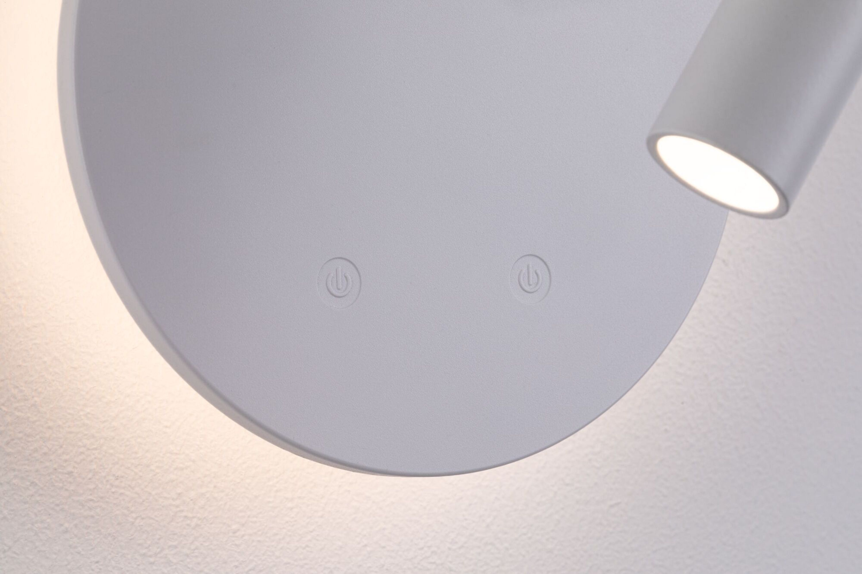 Biała lampa z okrągłą podstawą i cylindrycznym reflektorem. Symbole zasilania widoczne na podstawie.