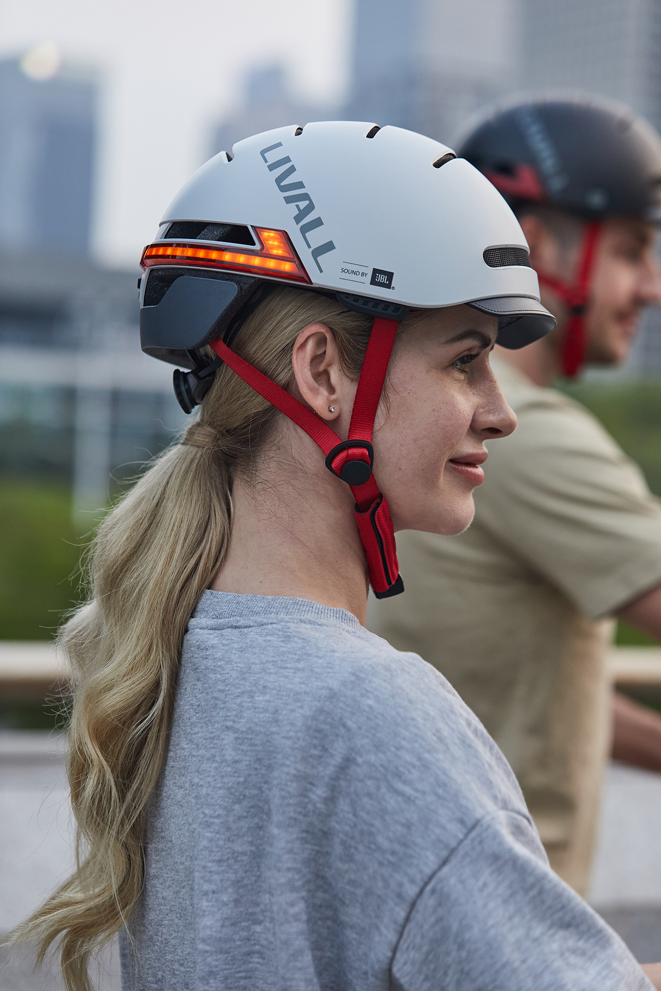 Eine Frau mit einem weißen LIVALL-Helm und roten Riemen. Eine weitere Person mit schwarzem Helm im Hintergrund.