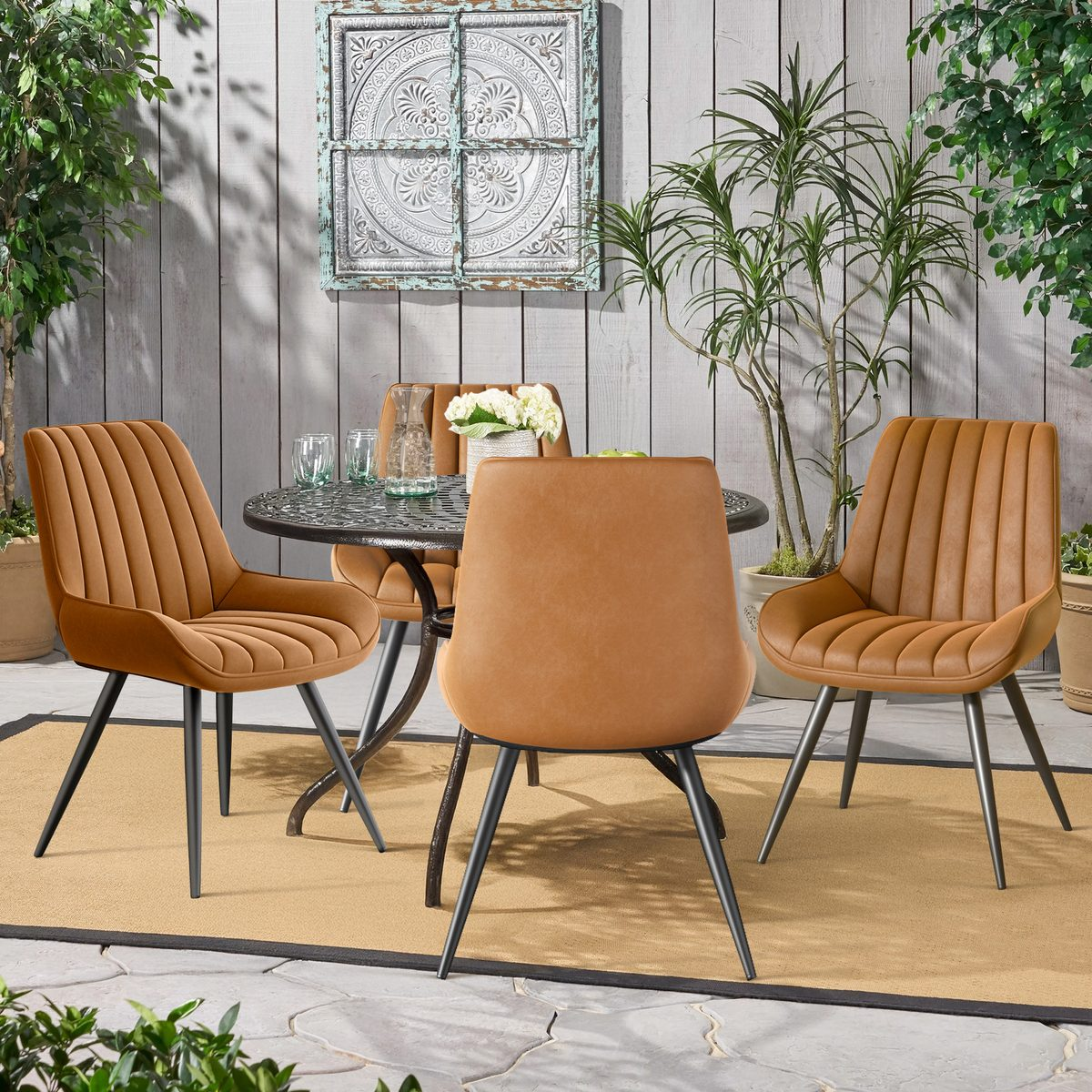 Essgruppe im Freien: Tisch, vier braune Stühle, Pflanzen und dekorative Wandkunst auf einer Terrasse. Die Stühle haben schwarze Beine.
