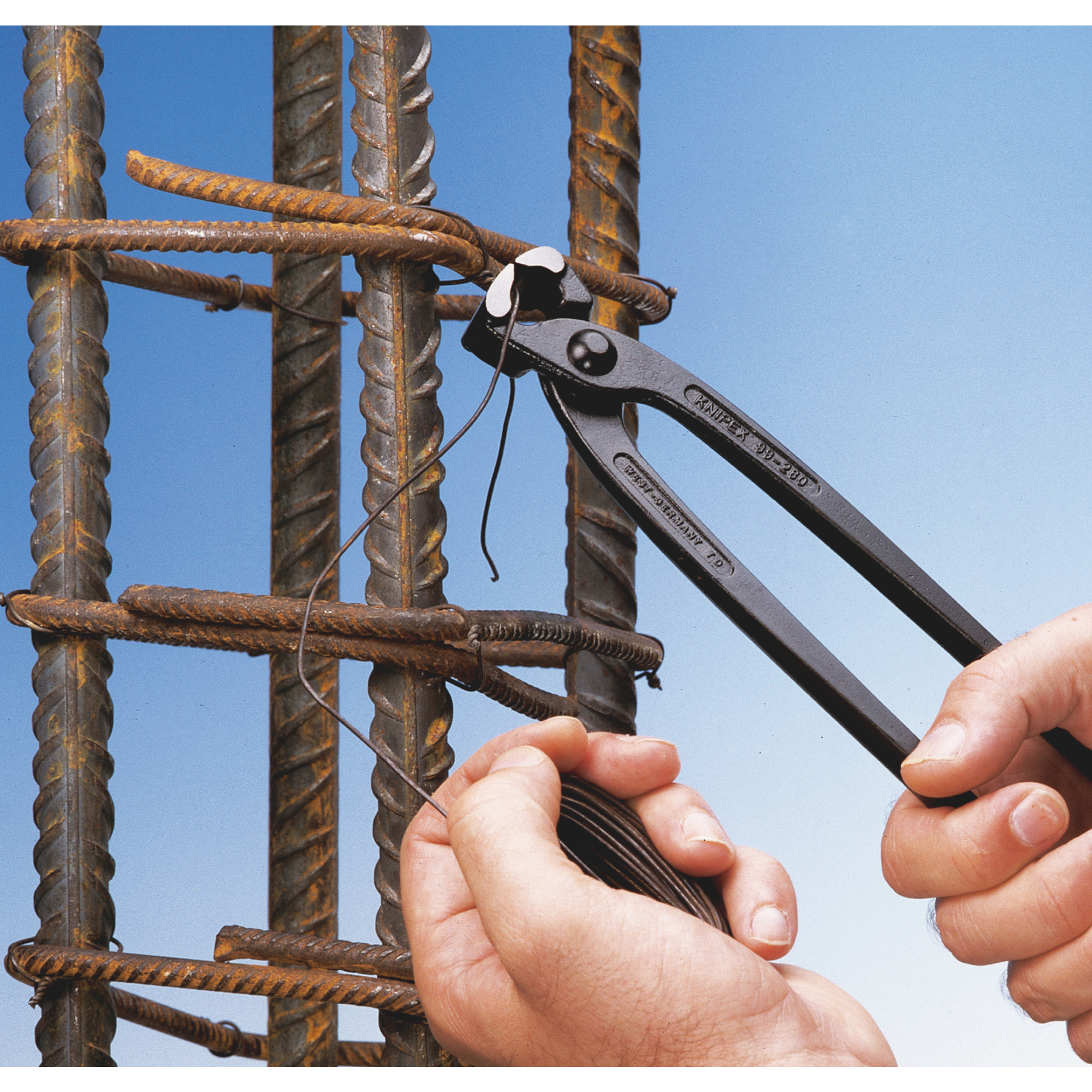 Ręce używają szczypiec do skręcania drutu wokół prętów zbrojeniowych. Czarne szczypce i brązowe pręty zbrojeniowe na niebieskim tle.