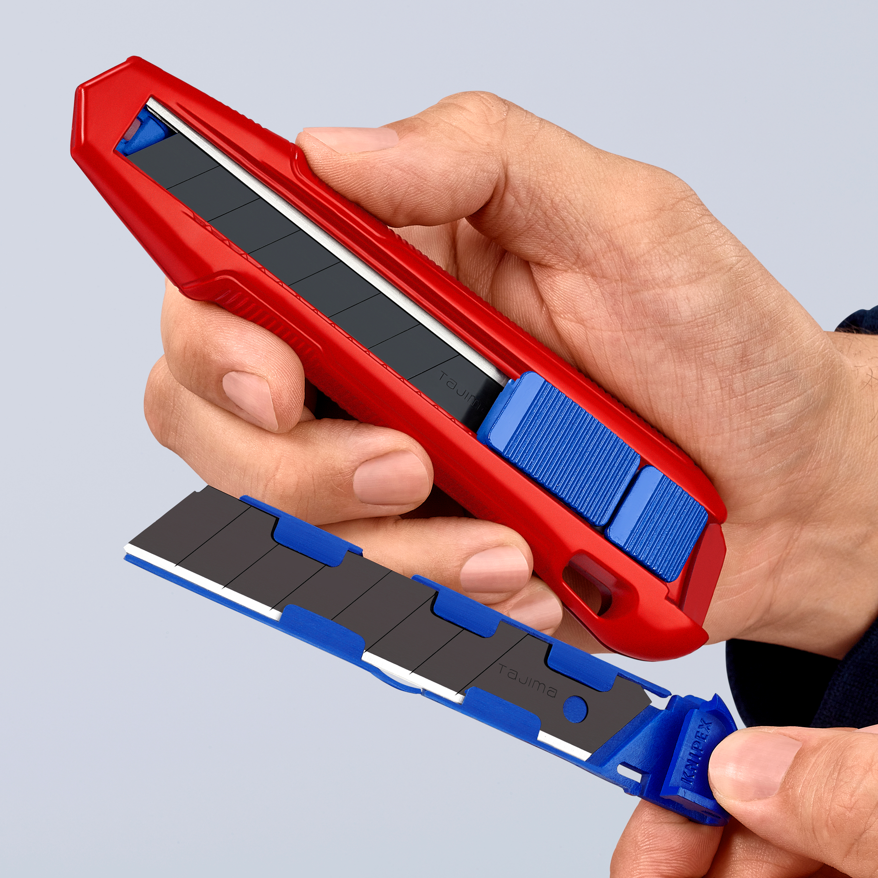 Eine Hand hält ein rotes und blaues Universalmesser mit abgetrennter Klinge. Die Klinge ist schwarz.
