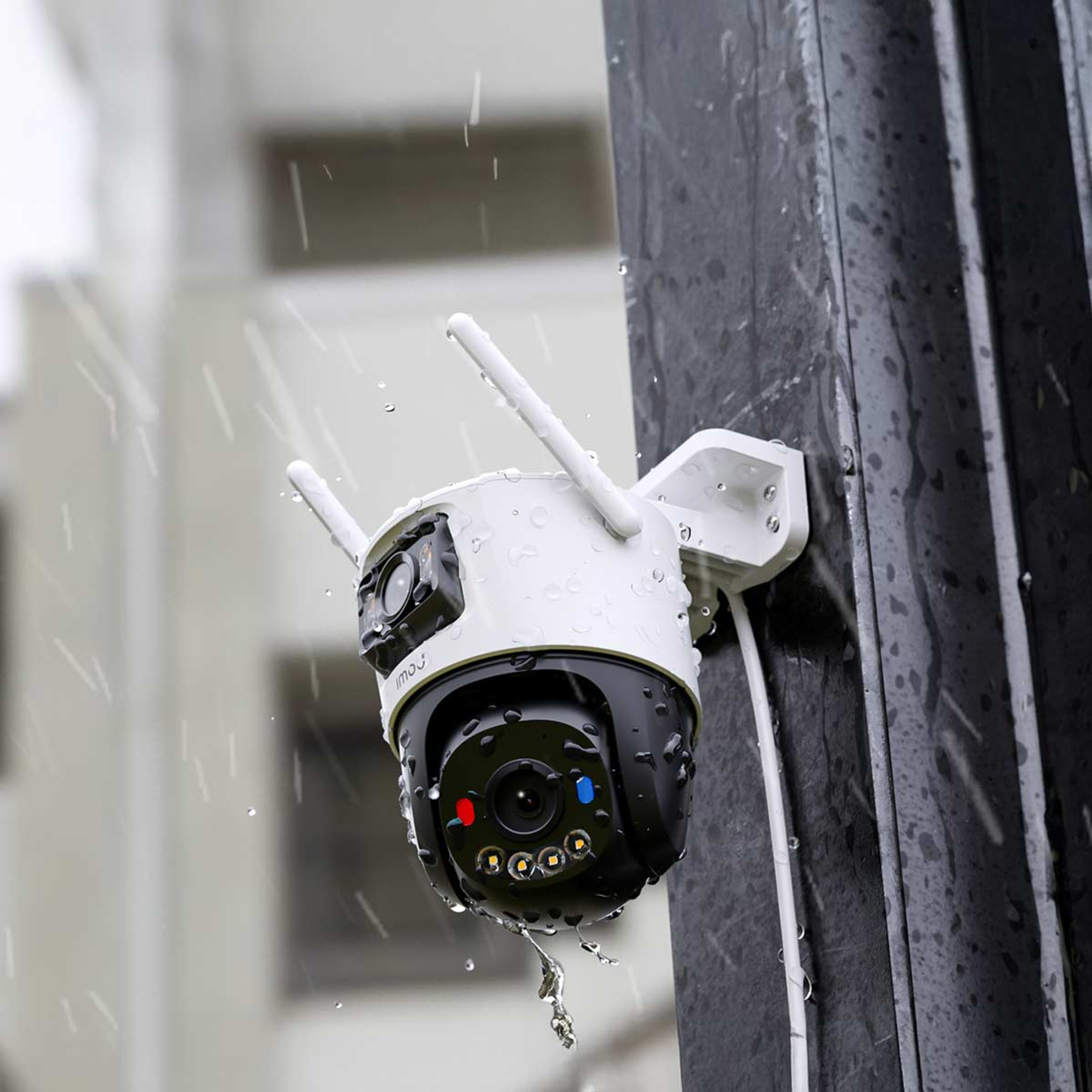 Biała i czarna kamera monitoringu z antenami, zamontowana na słupie, w deszczu. Widoczne krople wody.