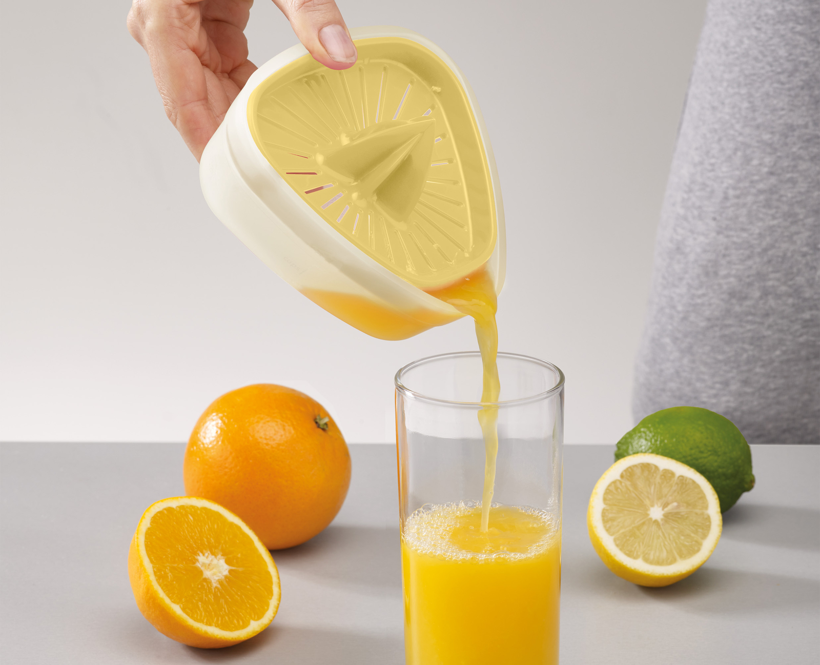 Mano che sprema succo in un bicchiere con uno spremiagrumi. Arance e limoni sul tavolo.