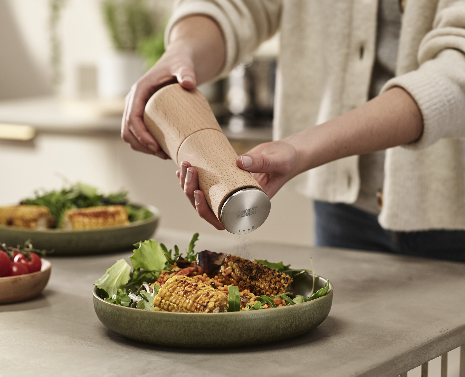 Una persona está moliendo pimienta sobre un plato de comida. El plato tiene maíz, ensalada y otros ingredientes.