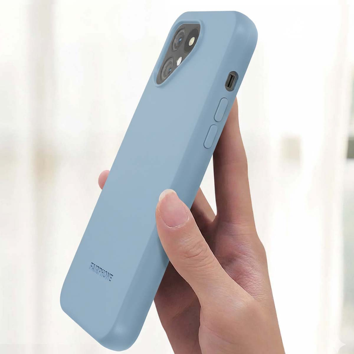 Una mano tiene una custodia per telefono azzurra. La custodia ha ritagli per la fotocamera e pulsanti. La parola FAIRPHONE è stampata.
