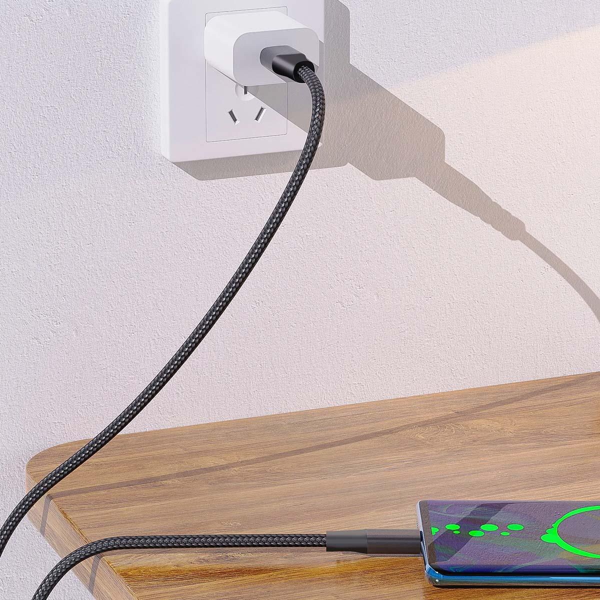 Telefon się ładuje. Czarny kabel łączy telefon z białą ładowarką wpiętą do gniazdka na drewnianej powierzchni.